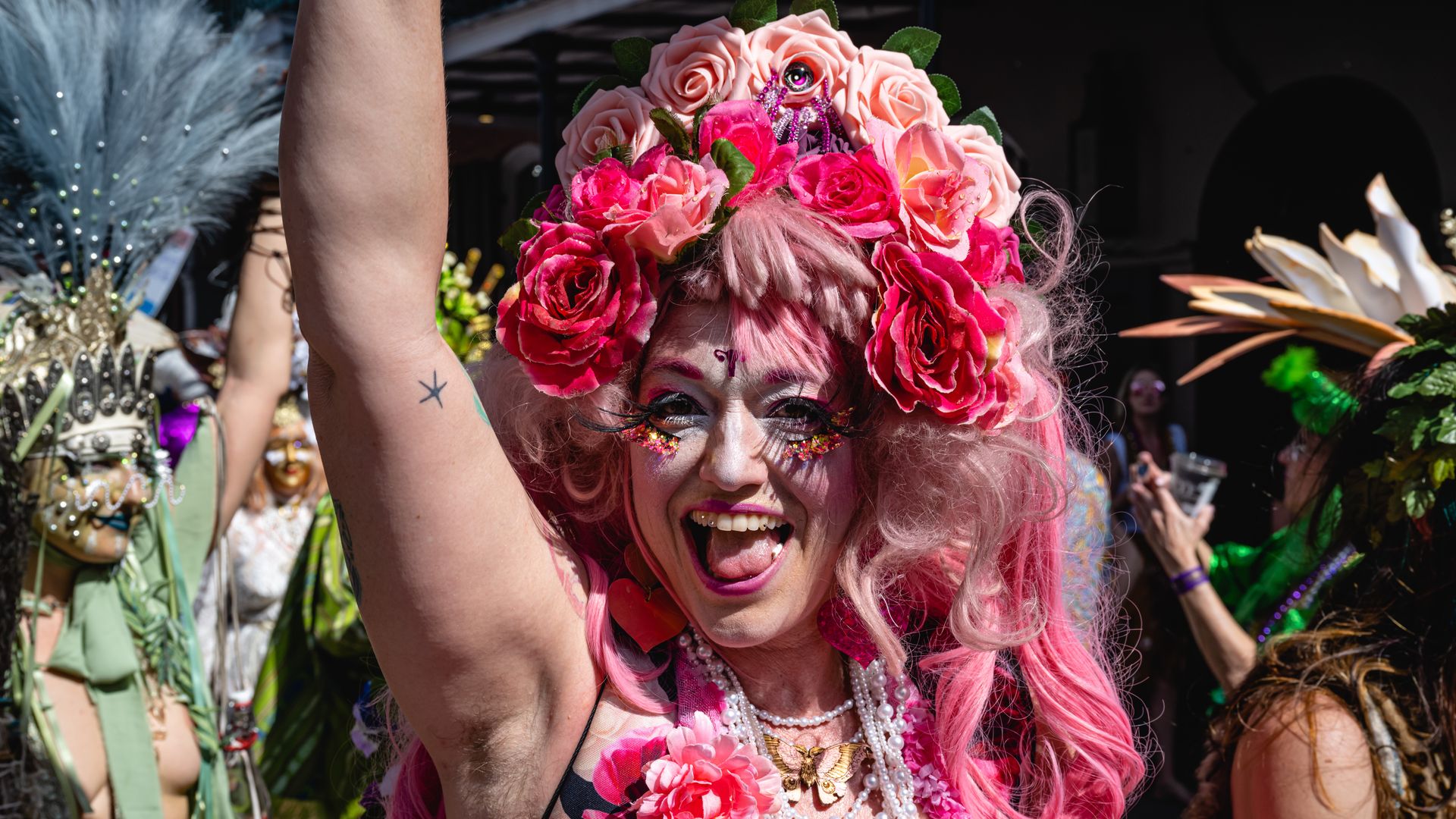 A costumed woman smiles at the camera wearing a bright pink floral headdress and a pink wig.