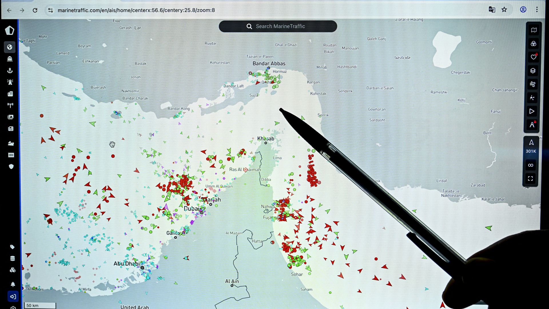 A person points at the Strait of Hormuz on a map with green and red symbols representing vessels with a mechanical pencil or a pen.