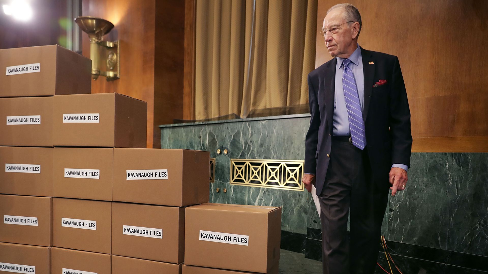 Chuck Grassley walking to the front of a pile of cardboard boxes labelled "Kavanaugh Files"