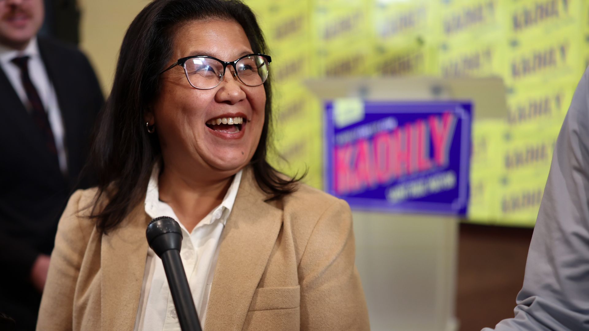 Kaohly Her in a tan blazer talking into a mic held by an arm