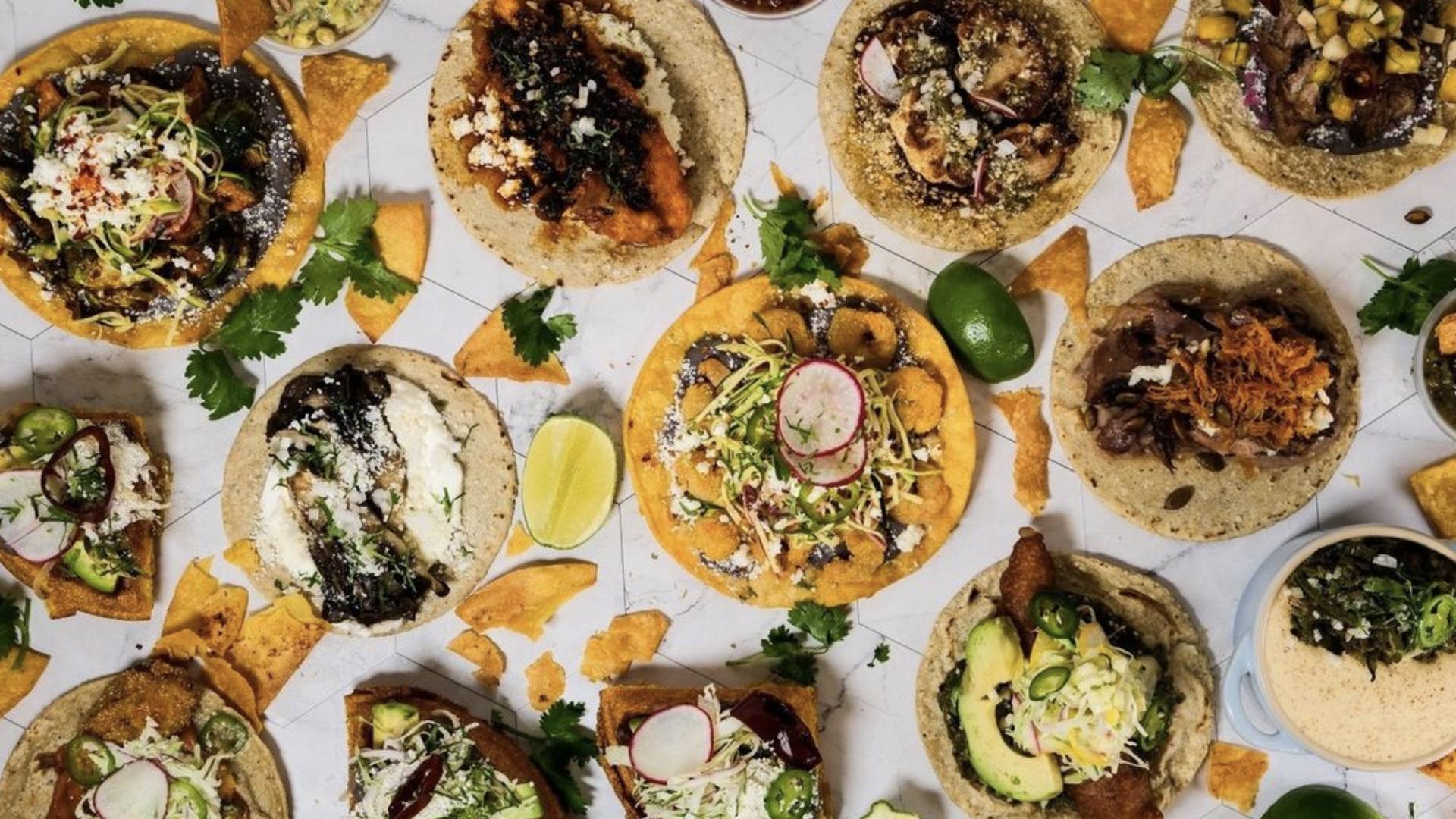 An overhead shot of tacos and huevos rancheros decorated with crisp yellow tostada chips