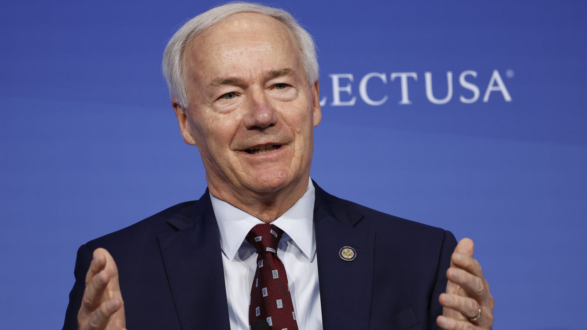 Gov. Asa Hutchinson of Arkansas speaks from a stage with both hands in the air. 