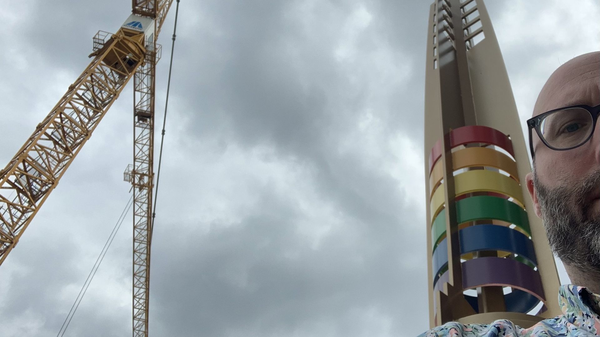Photo of a man in front of a pillar and a construction crane. 