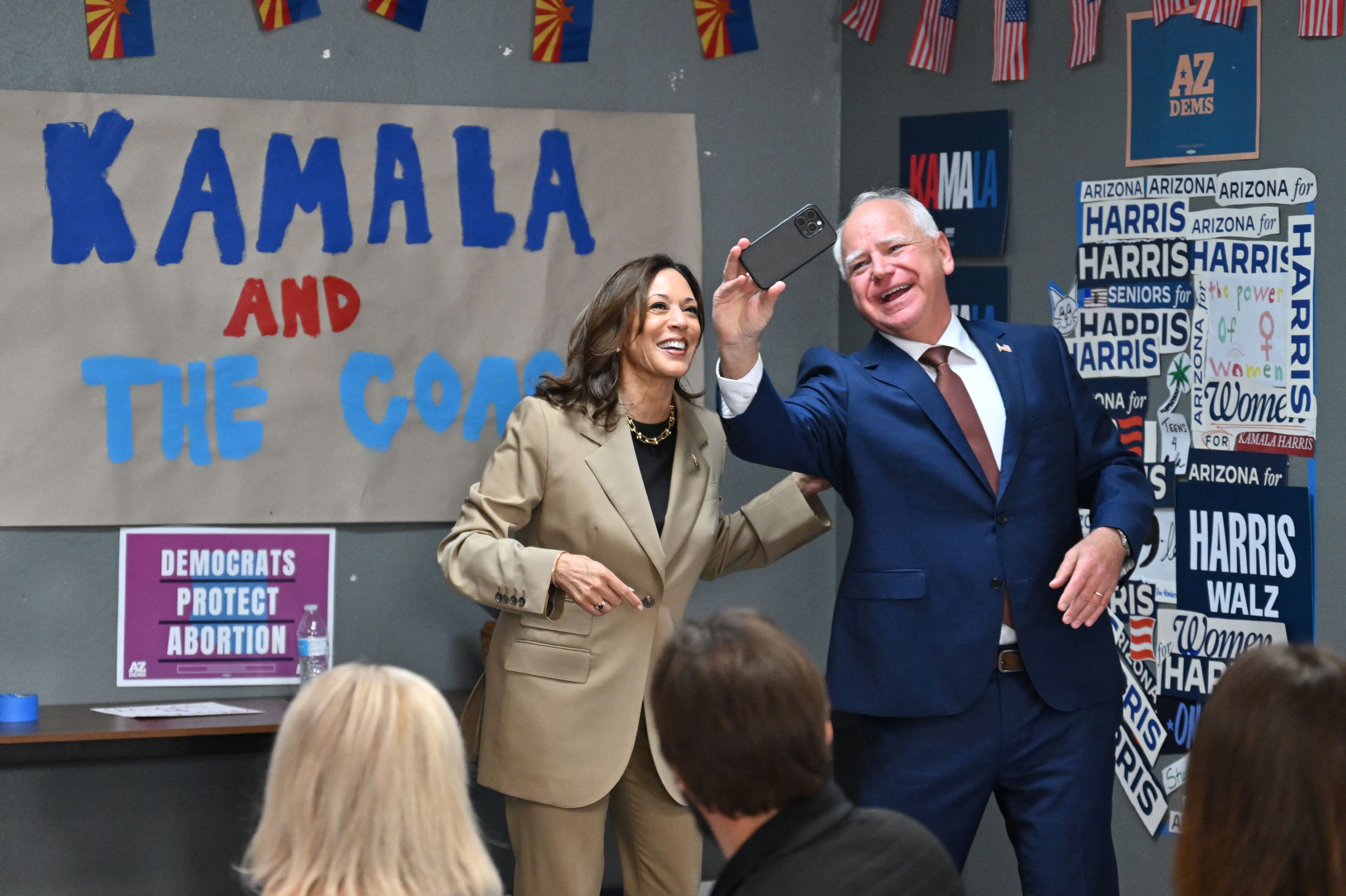 kamala Harris and Minnesota Governor and 2024 Democratic vice presidential candidate Tim Walz take a selfie in front of the "Kamala and the Coach" sign