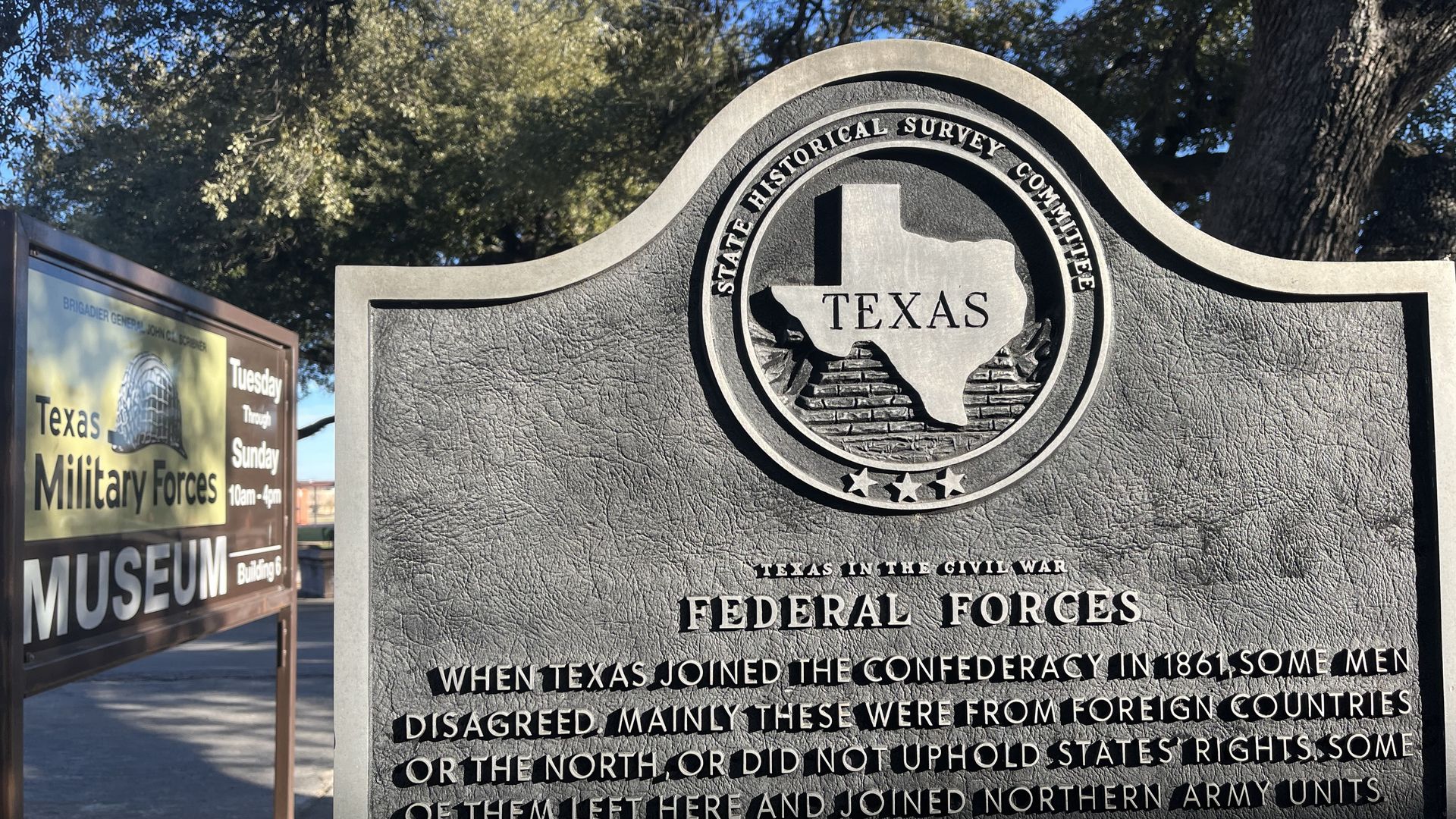 Historical Texas plaque detailing Federal Forces in the Civil War, near Texas Military Forces Museum sign, surrounded by trees under a clear blue sky.