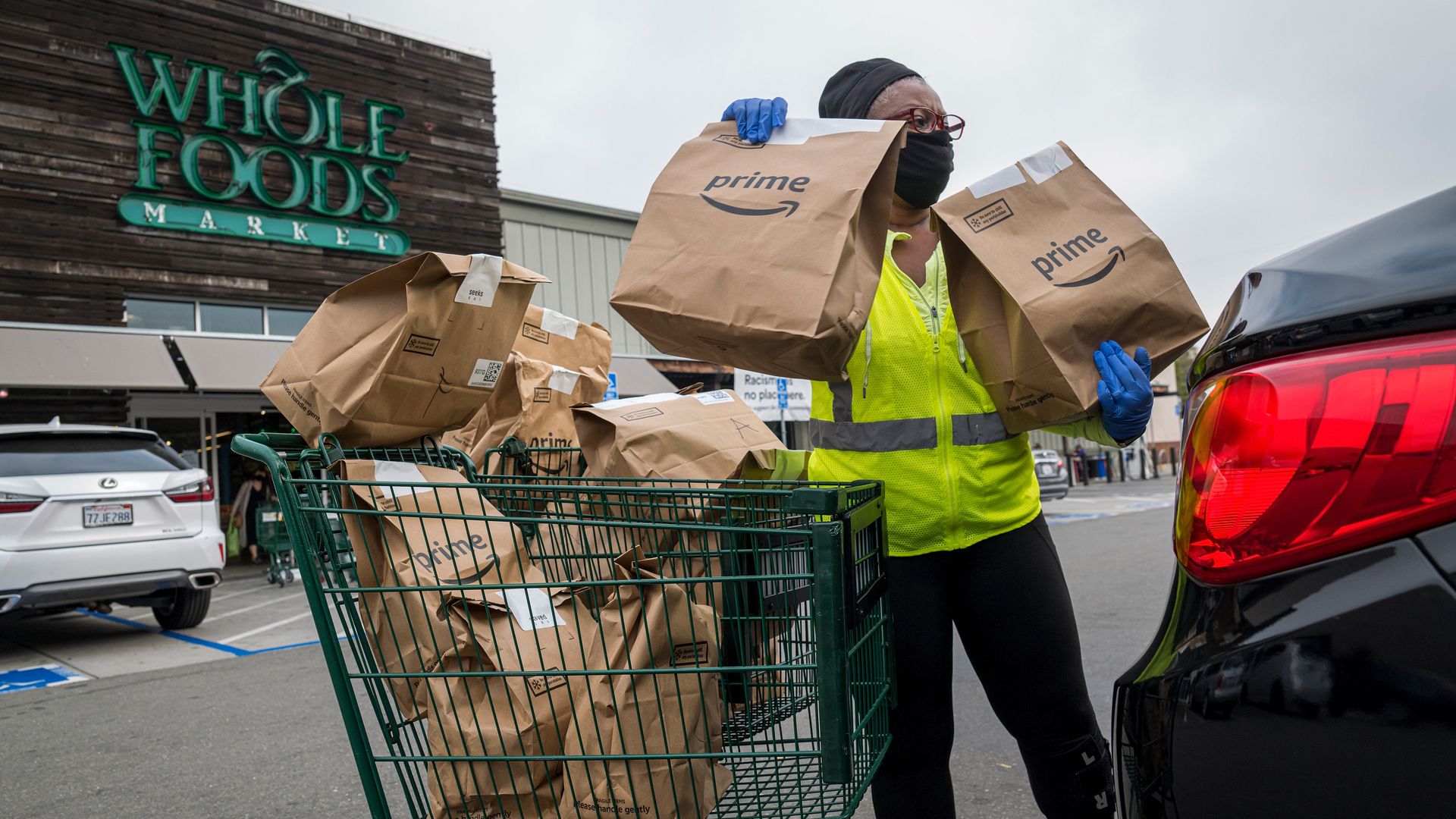 A woman loads Amazon Prime grocery bags into a car outside of a Whole Foods store.
