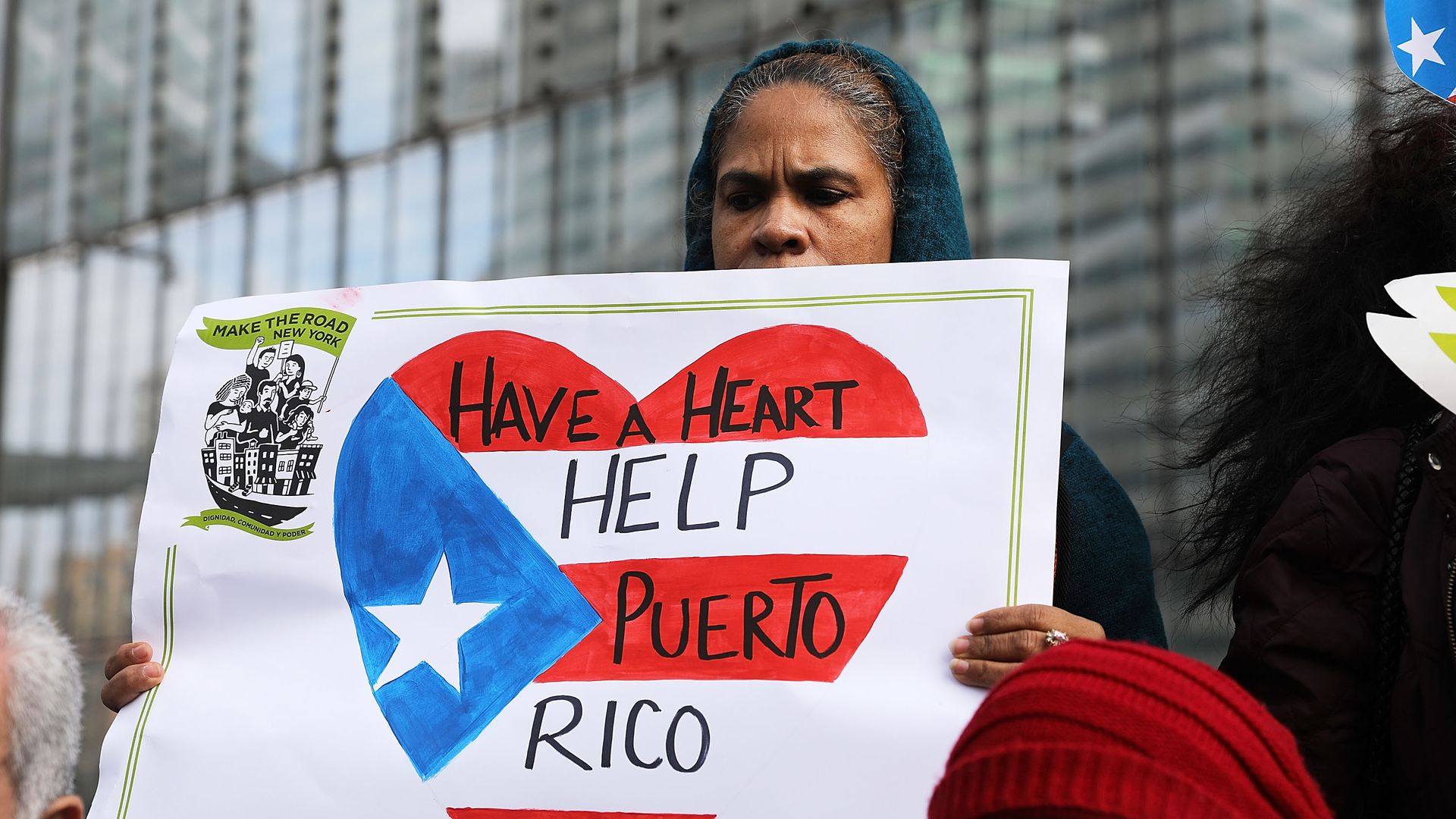 Woman holding a sign with an american flag heart which says "have a heart help puerto rico"