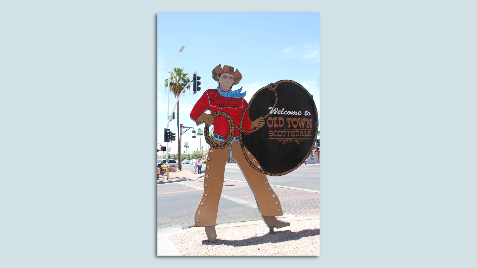 A giant metal cutout of a cowboy in tan chaps, a red shirt and cowboy hat holding a lasso in one hand, with the rope circling a sign that says "Welcome to Old Town Scottsdale."  