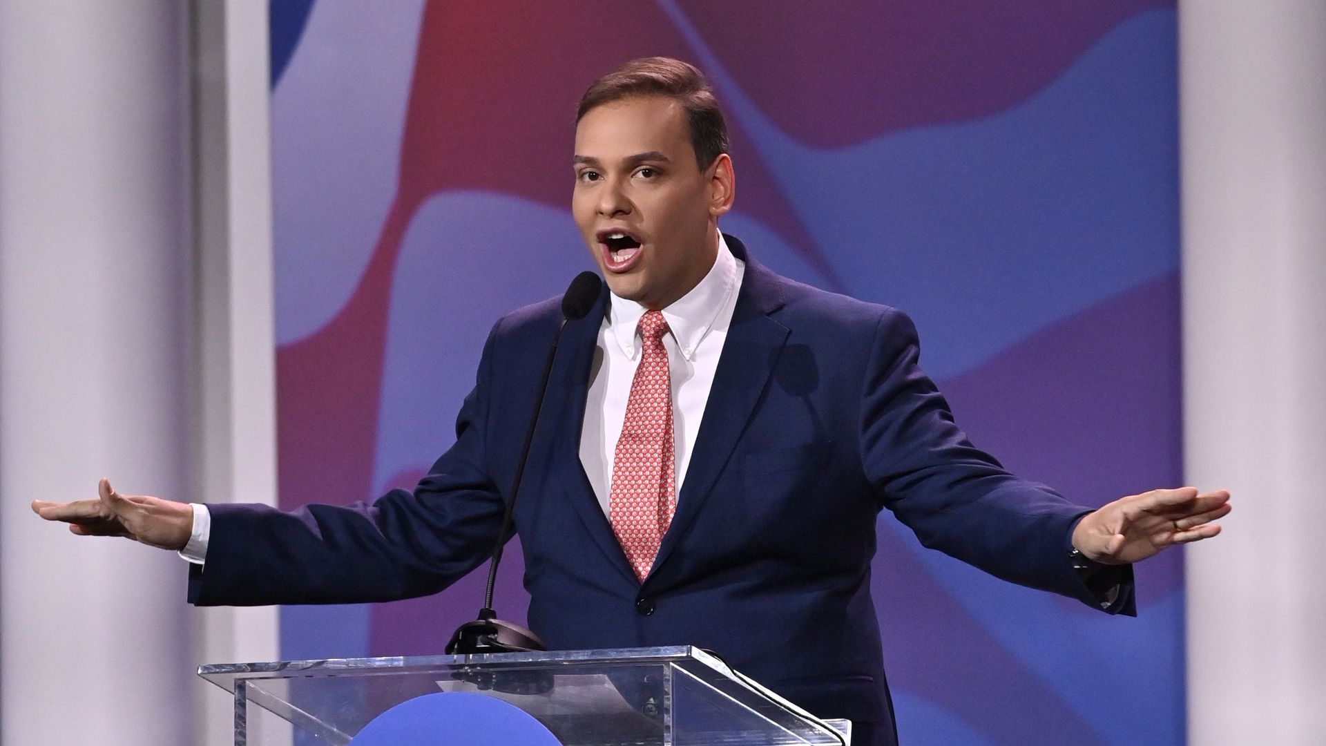 Rep-elect George Santos, wearing a blue suit, white shirt and pink tie, speaks to the Republican Jewish Coalition.
