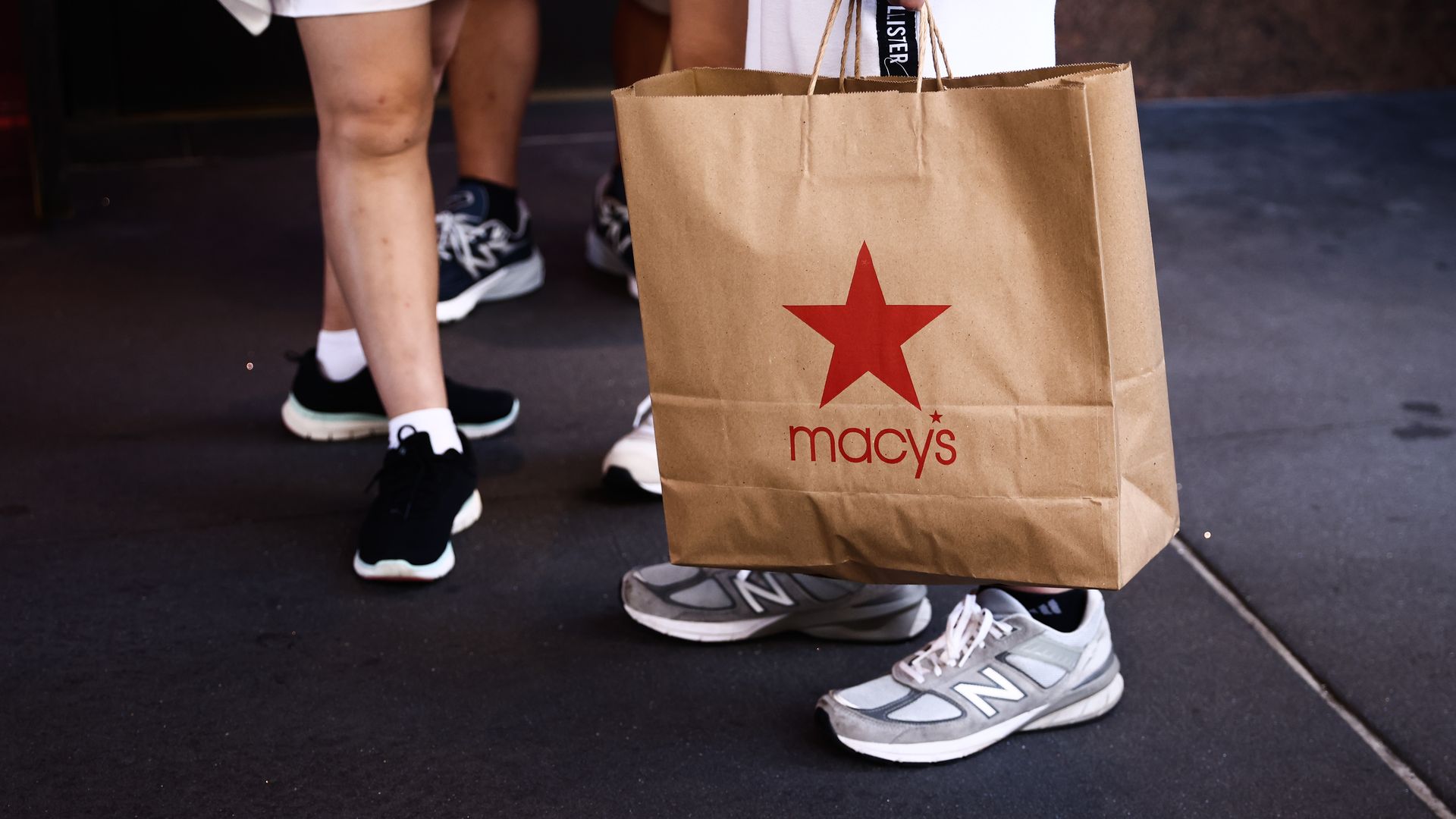 Customer holds brown paper shopping bag emblazoned with Macy's logo.