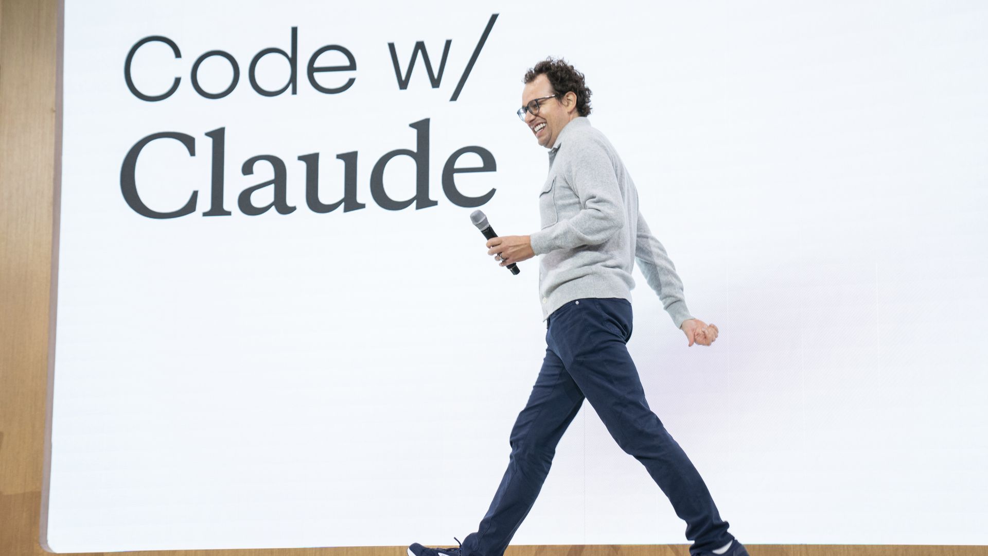 Dario Amodei strides onstage with "Code w/ Claude" projected behind him.