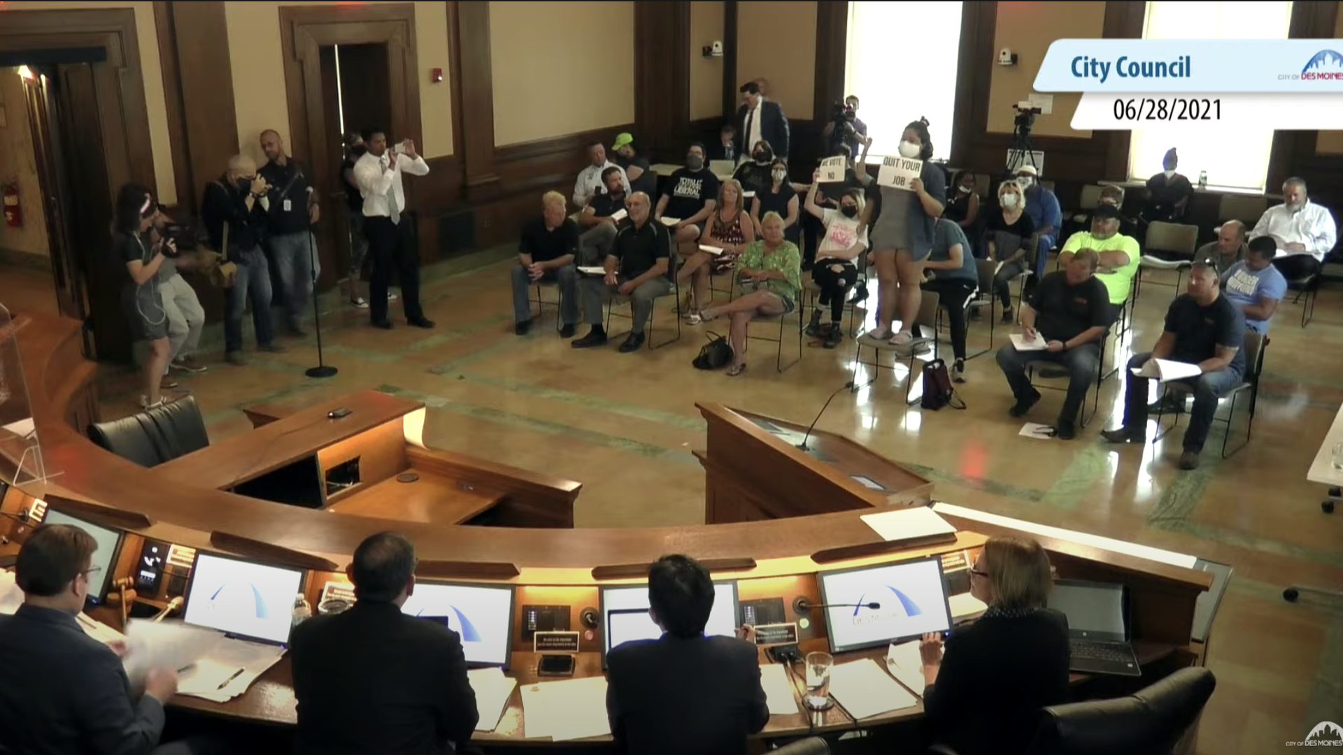 Protesters stand with signs at the Des Moines City Council meeting on June 28, 2021.