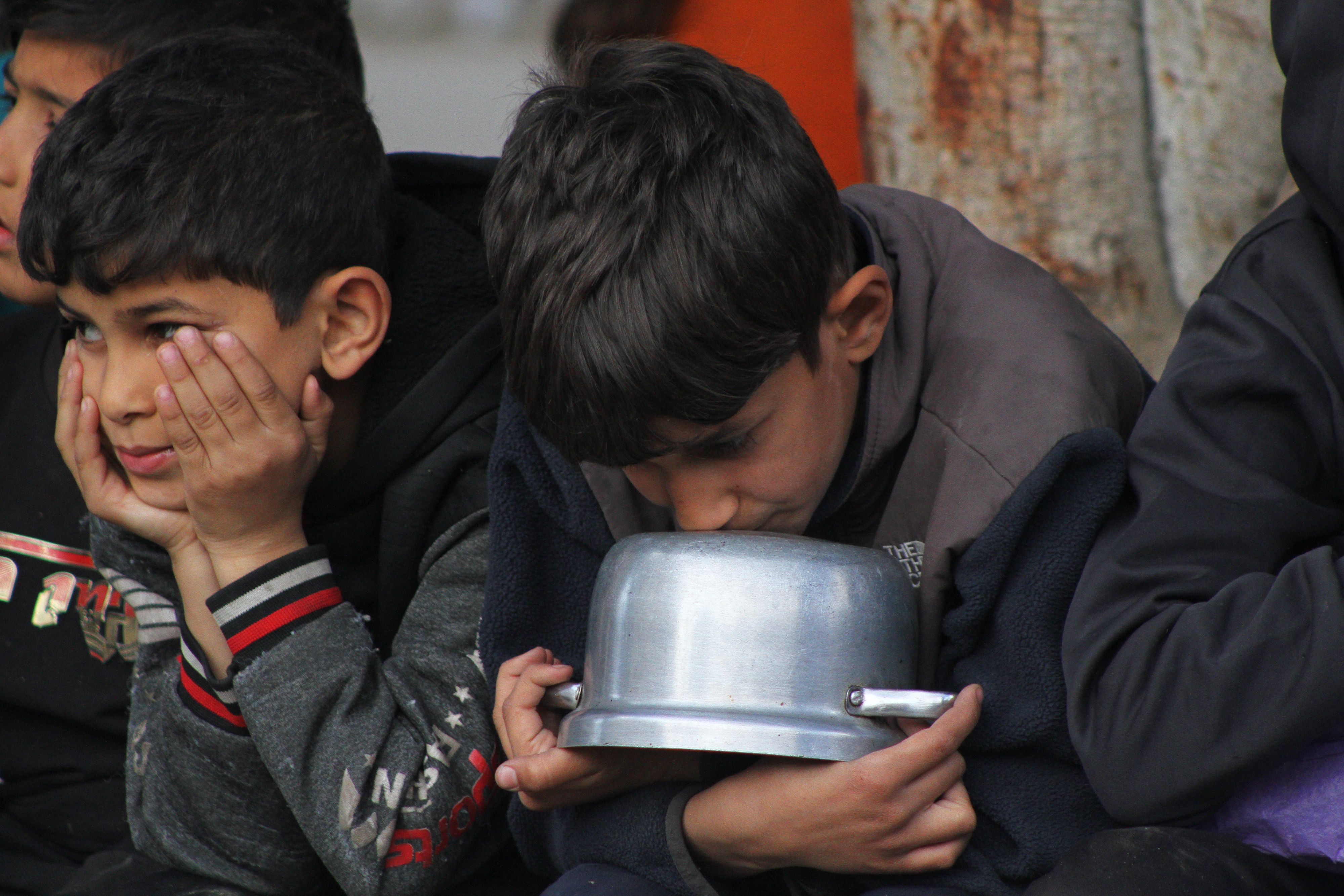 Children sit together holding empty pots.