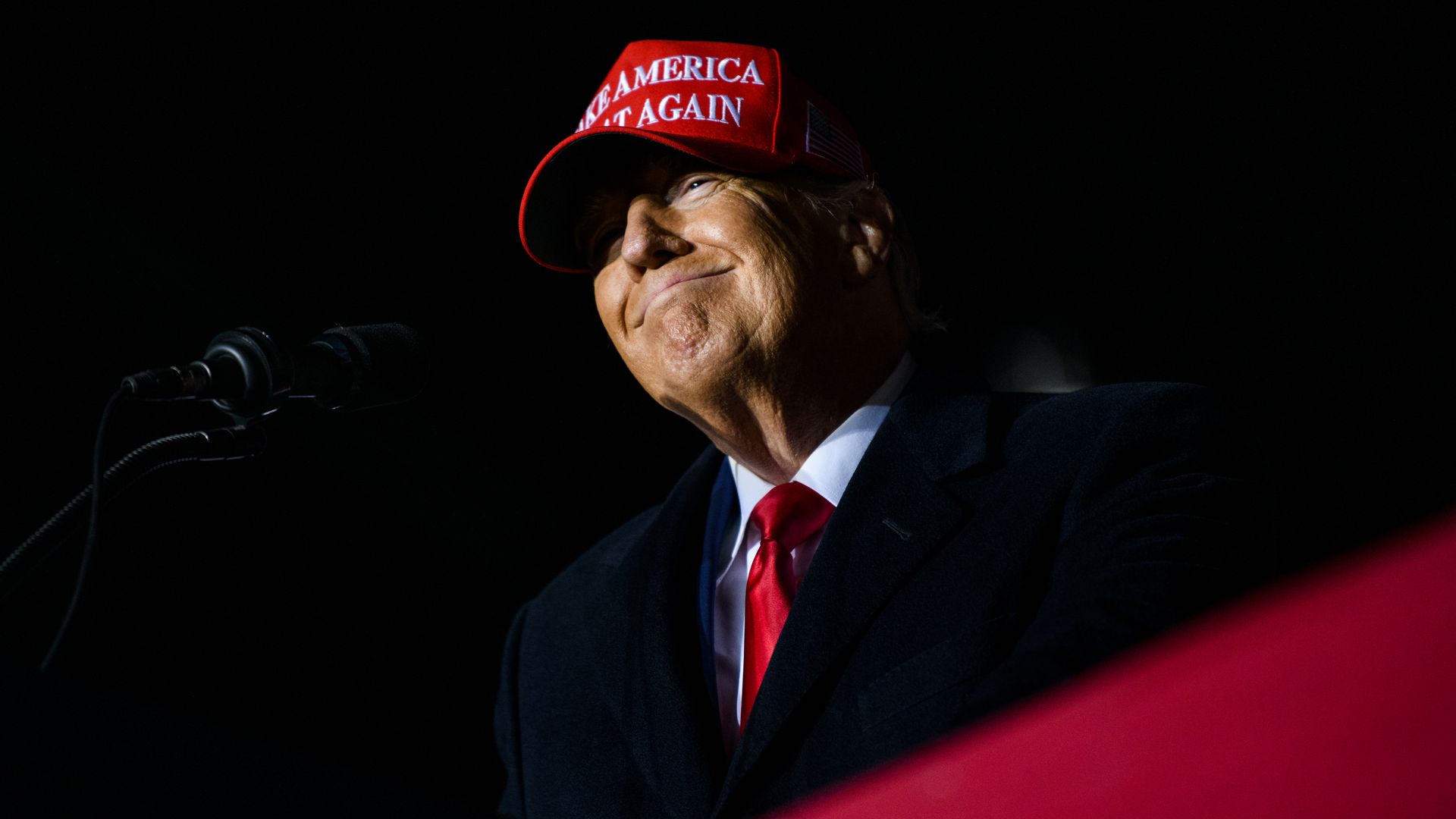 President Trump smiles while wearing a MAGA hat at a rally. 