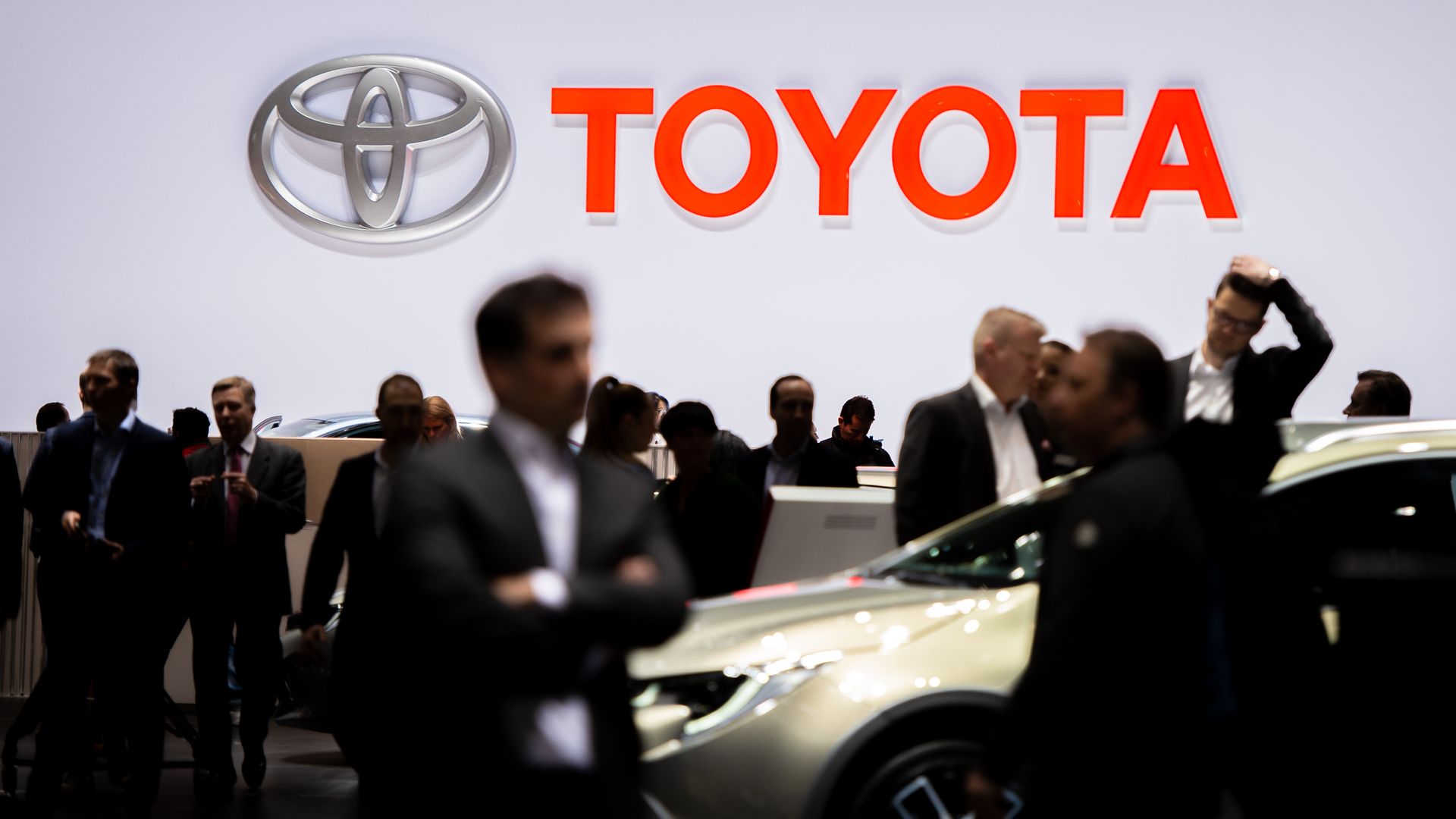 In this image, crowds of mostly suited people walk around a show floor with the Toyota logo overhead. 