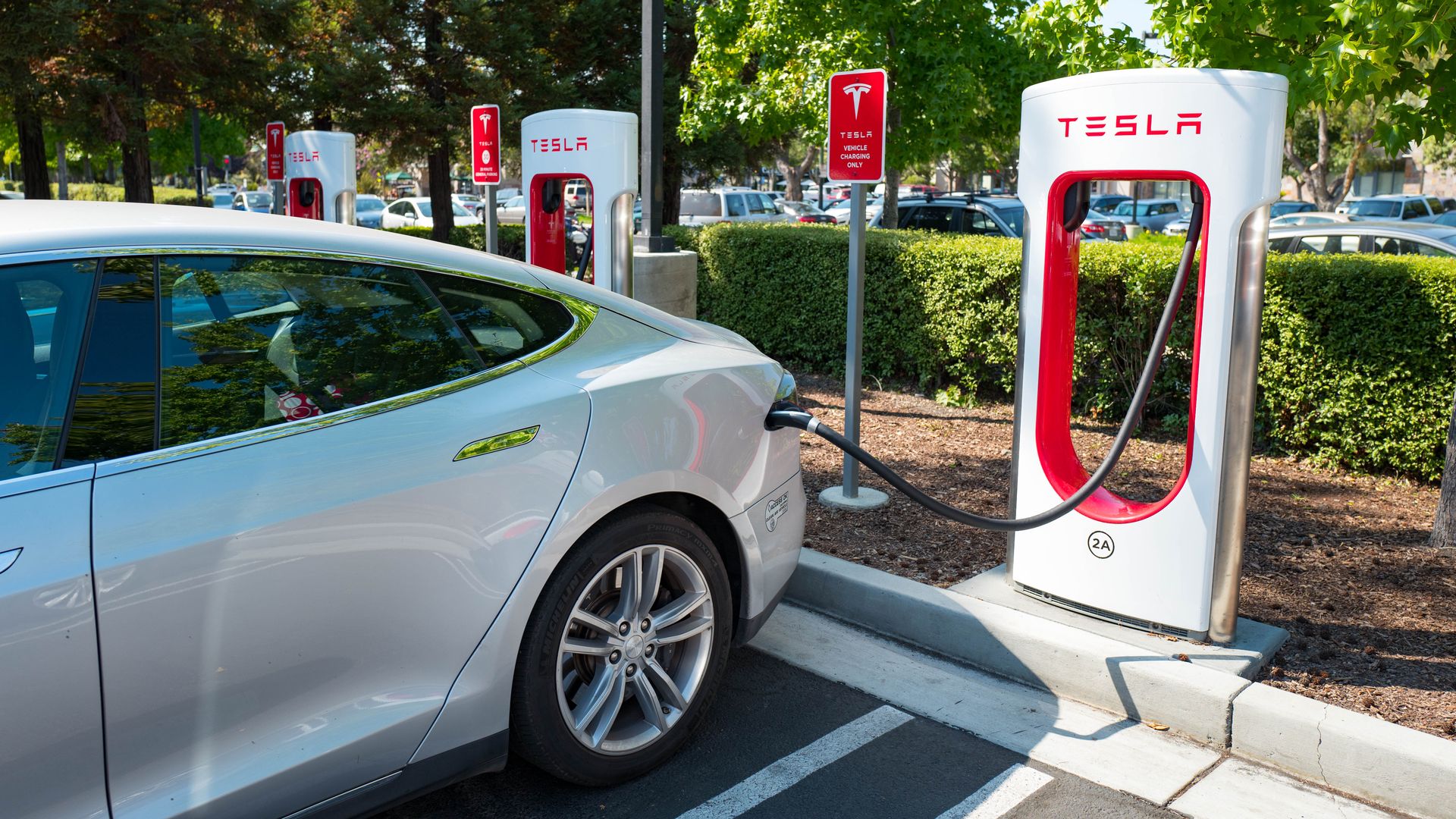 In this image, a silver sedan is charged at a Tesla port in a parking lot.