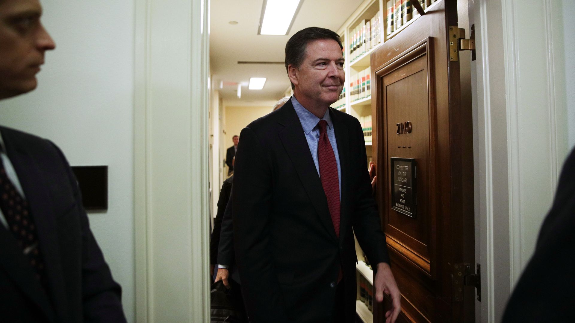 In this image, Comey walks out of a door