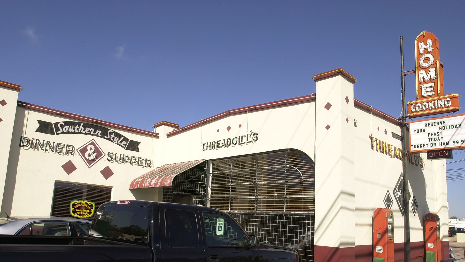 Exterior of Threadgill's Southern style dinner and supper restaurant with a black pickup parked outside, white and maroon building, clear blue sky, and a sign reading "HOME COOKING".