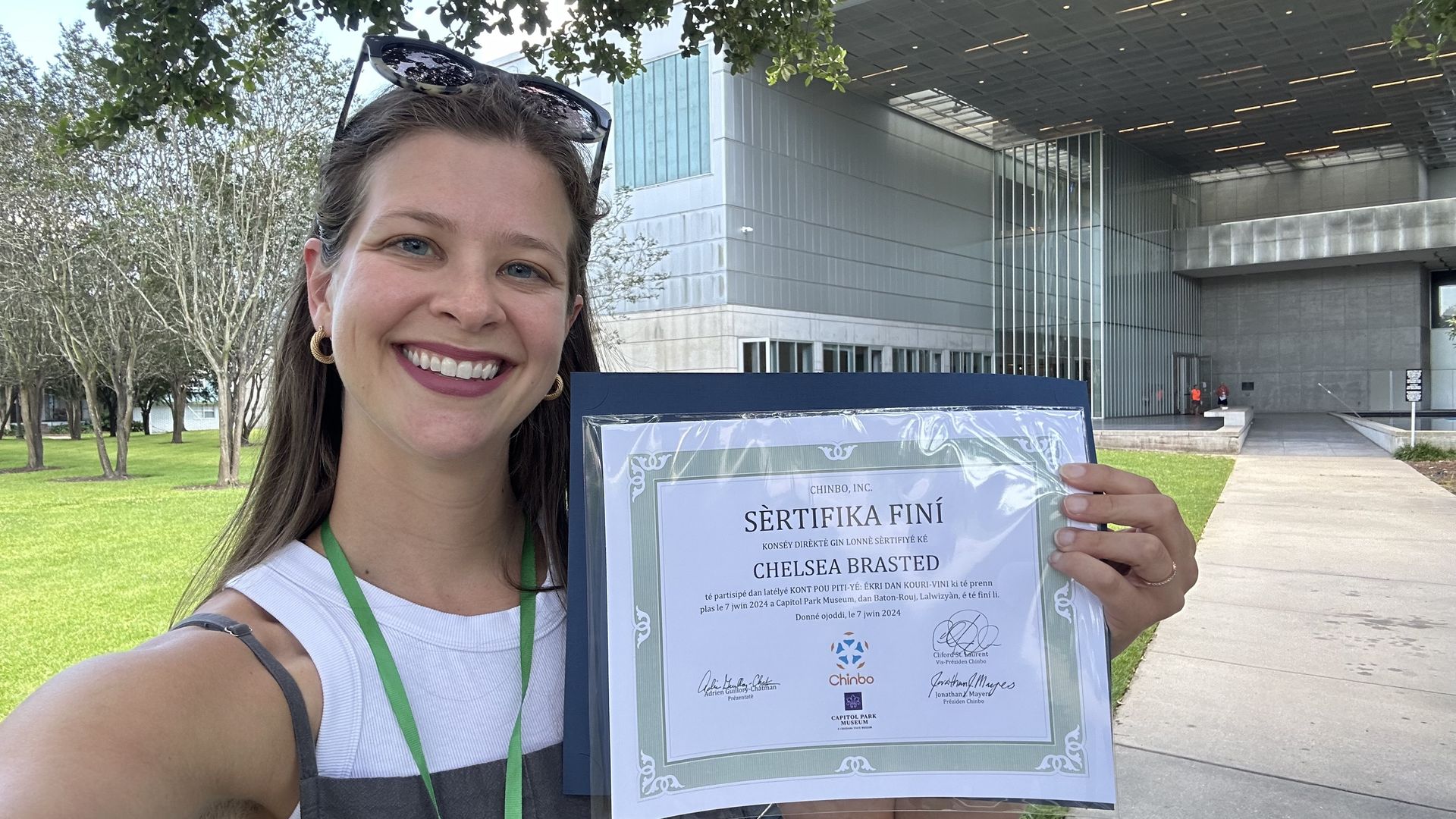 A selfie with a woman smiling at the camera and holding up a certificate that says "SÉRTIFIKA FINÍ."