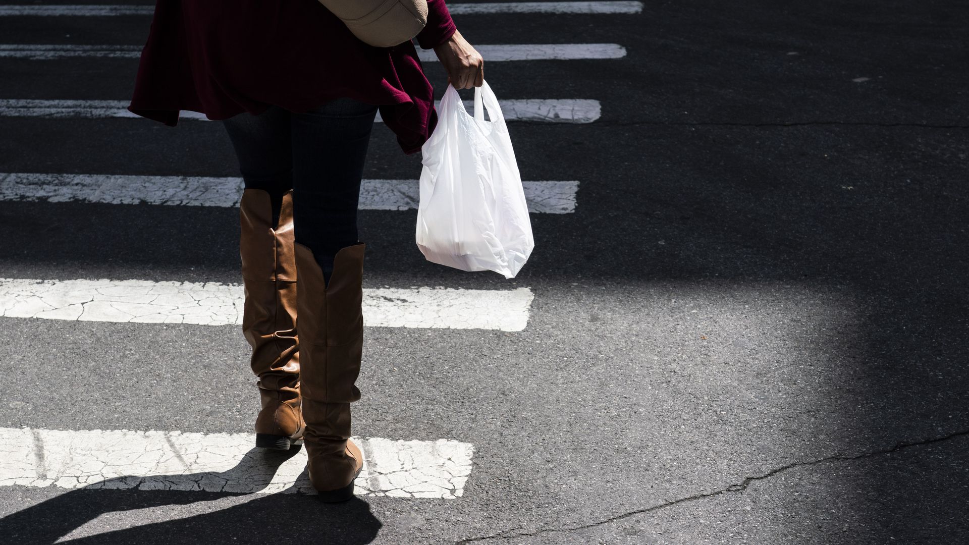 A photo of a person's legs walking along a crosswalk with a plastic shopping bag in their right hand