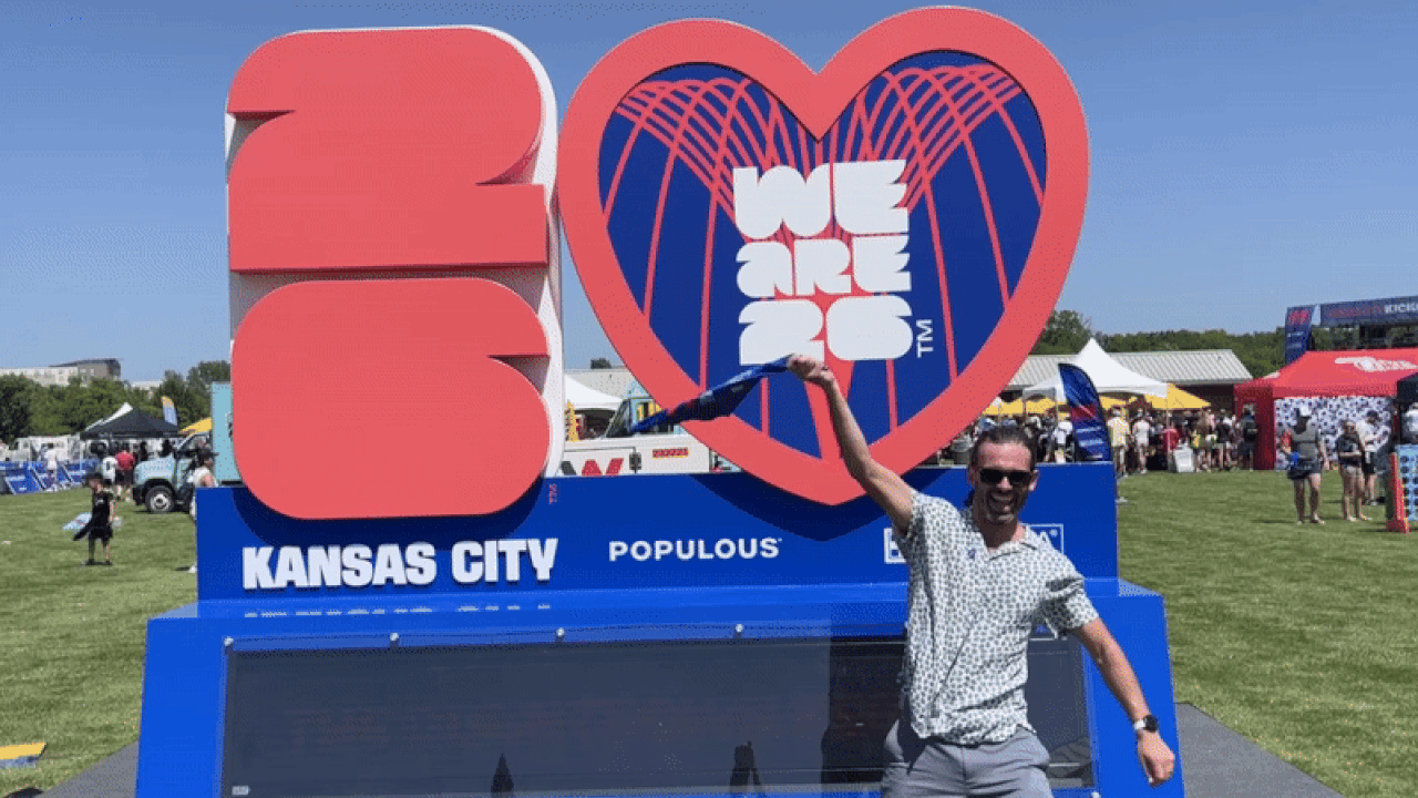 Reporter Travis Meier waves a World Cup 2026 rally flag in front of the countdown clock at the kickoff event in Overland Park.