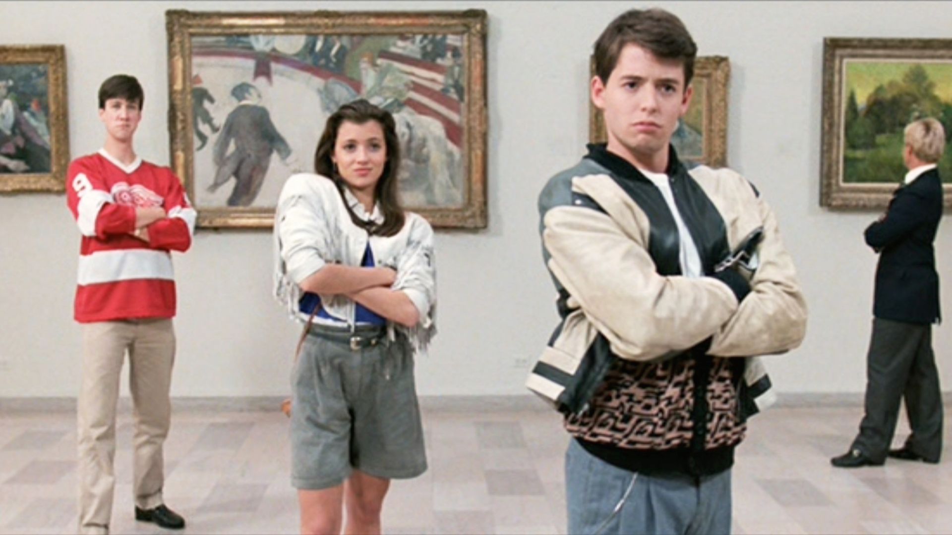 Three people pose in a museum gallery before framed paintings: left a teen in a red hockey jersey with arms crossed, center a woman in a white jacket and gray shorts, right a man in a beige and black jacket; a suited man observes art in the background.