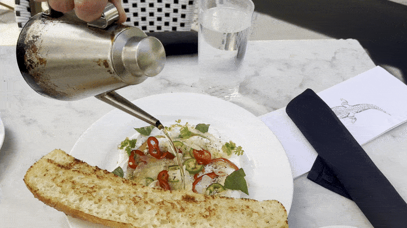 Image shows a video of someone pouring hot oil over a plate of white cheese and bread.