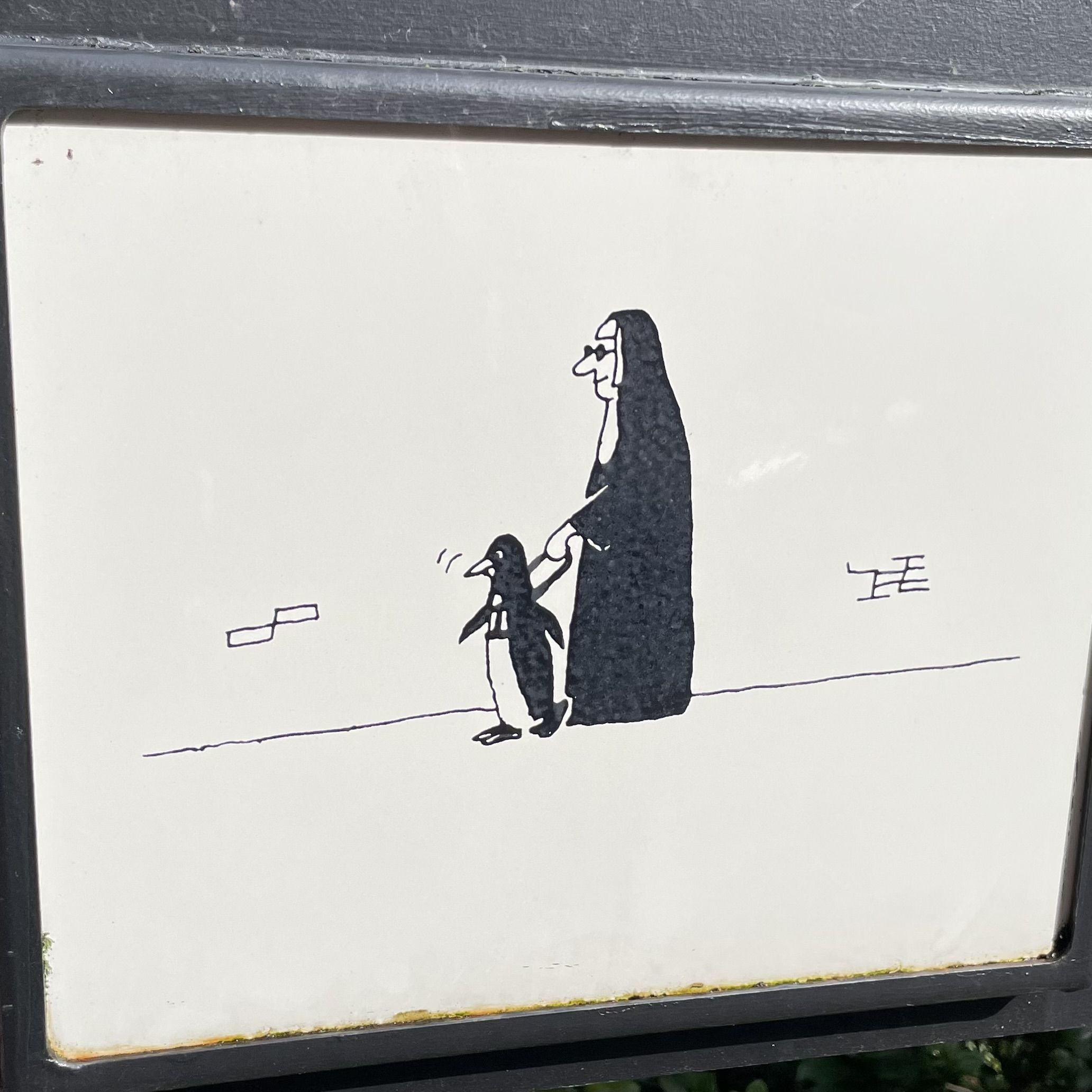 Simple black and white drawing of a person in a long black cloak holding hands with a small penguin, walking together on a plain white background with minimal line details.