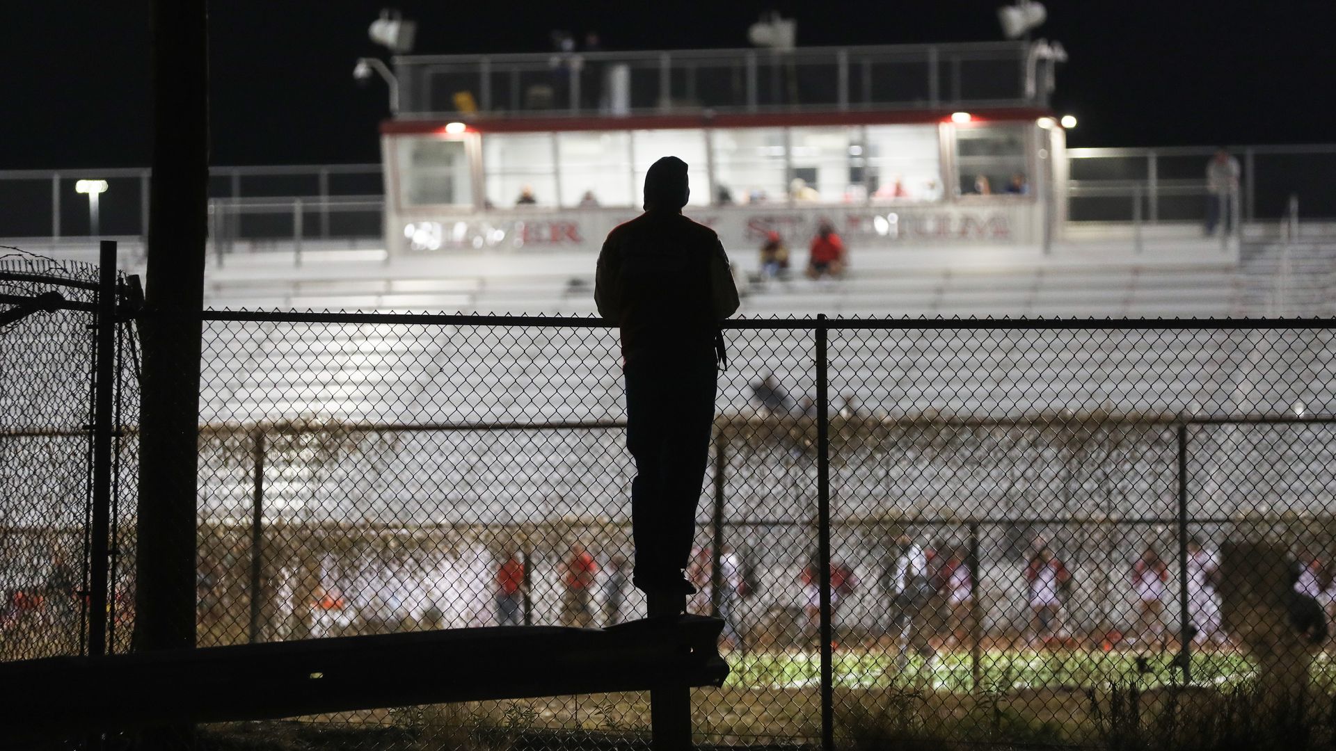 man watches hs football game over a fence