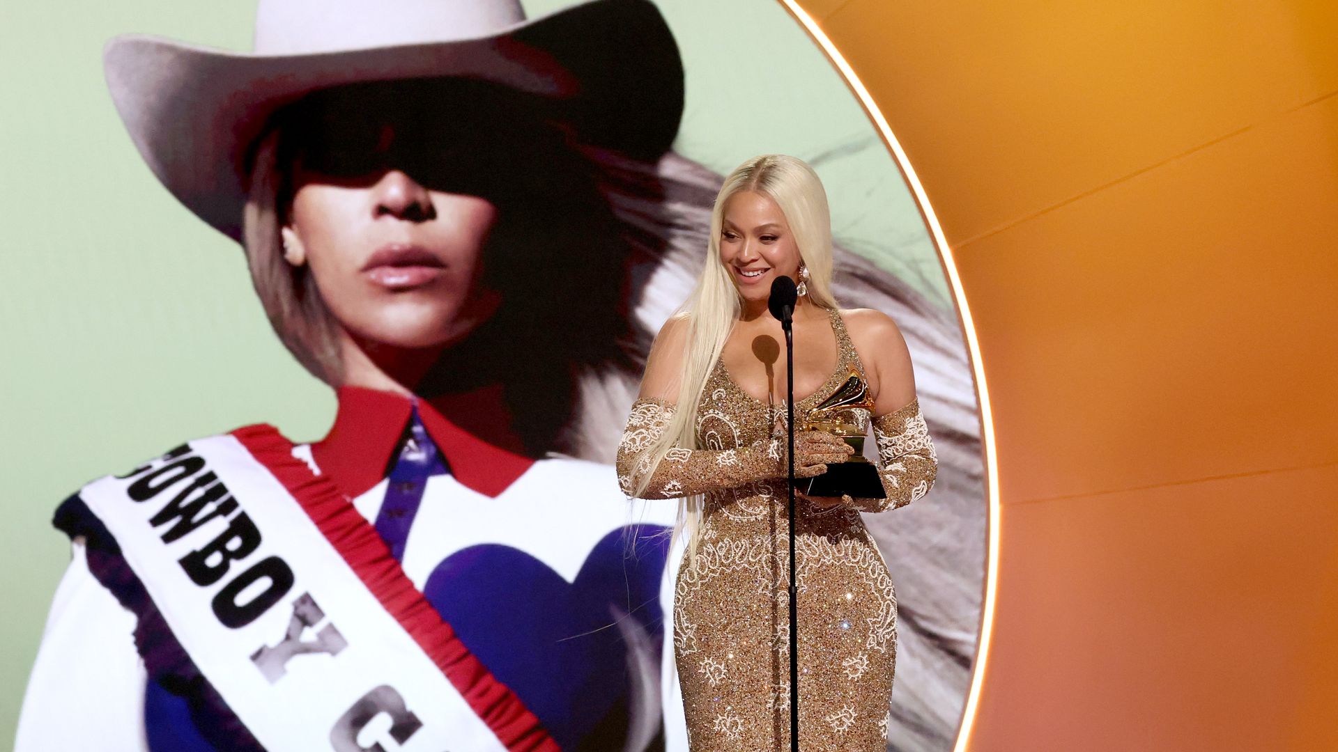 Photo of Beyonce accepting a Grammy with the album art of Cowboy Carter behind her. 