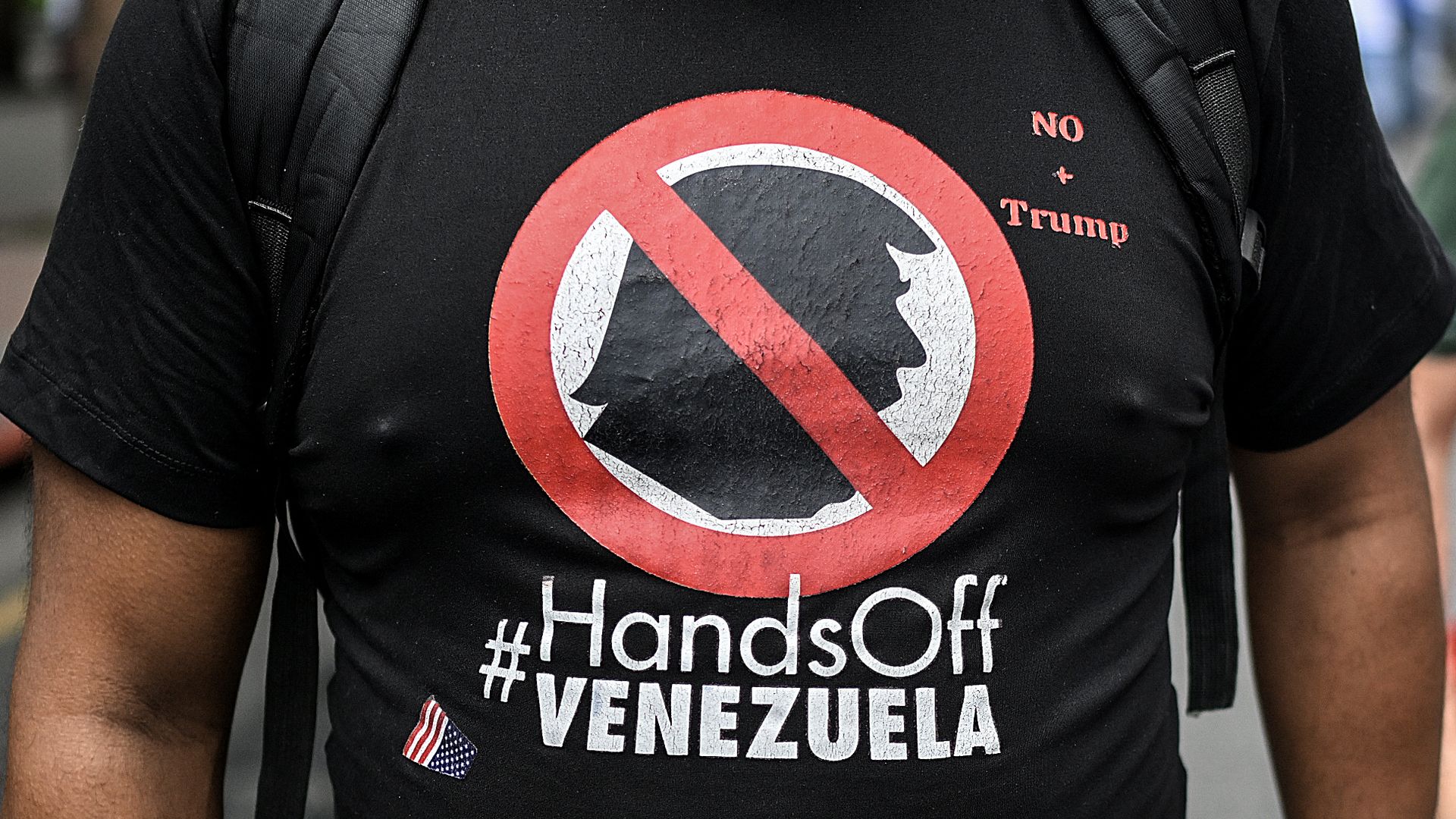 A person, whose face is not visible, wears a black shirt with a red slash through Trump's silhouette and the words #HandsOffVenezuela. 