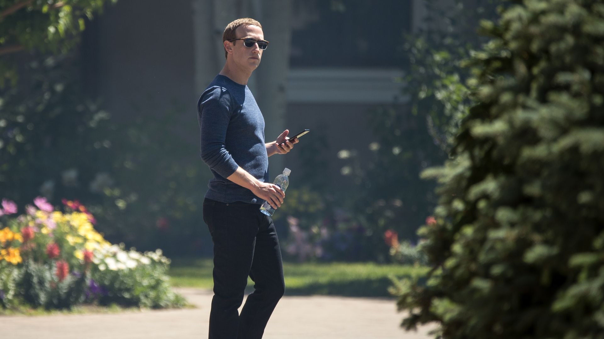 Mark Zuckerberg stands outside holding his phone