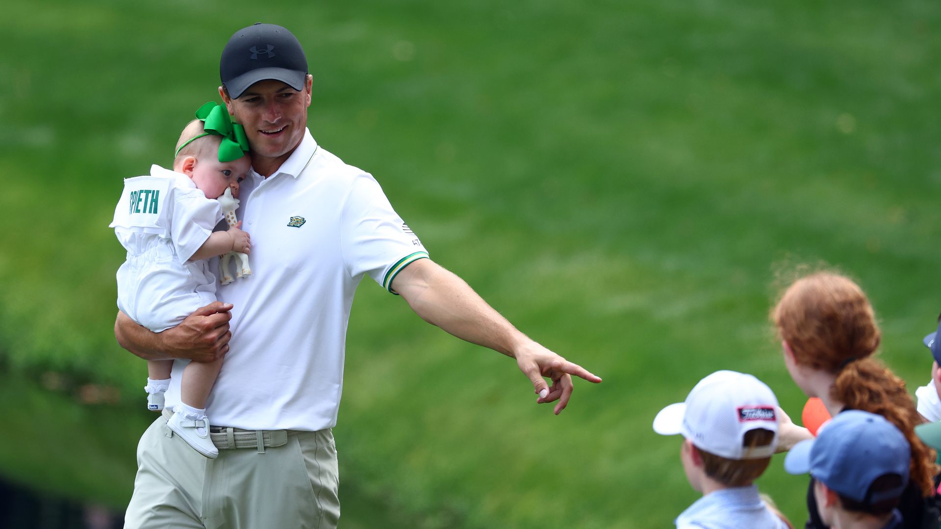 A golfer holds his infant daughter in his arms while on a green