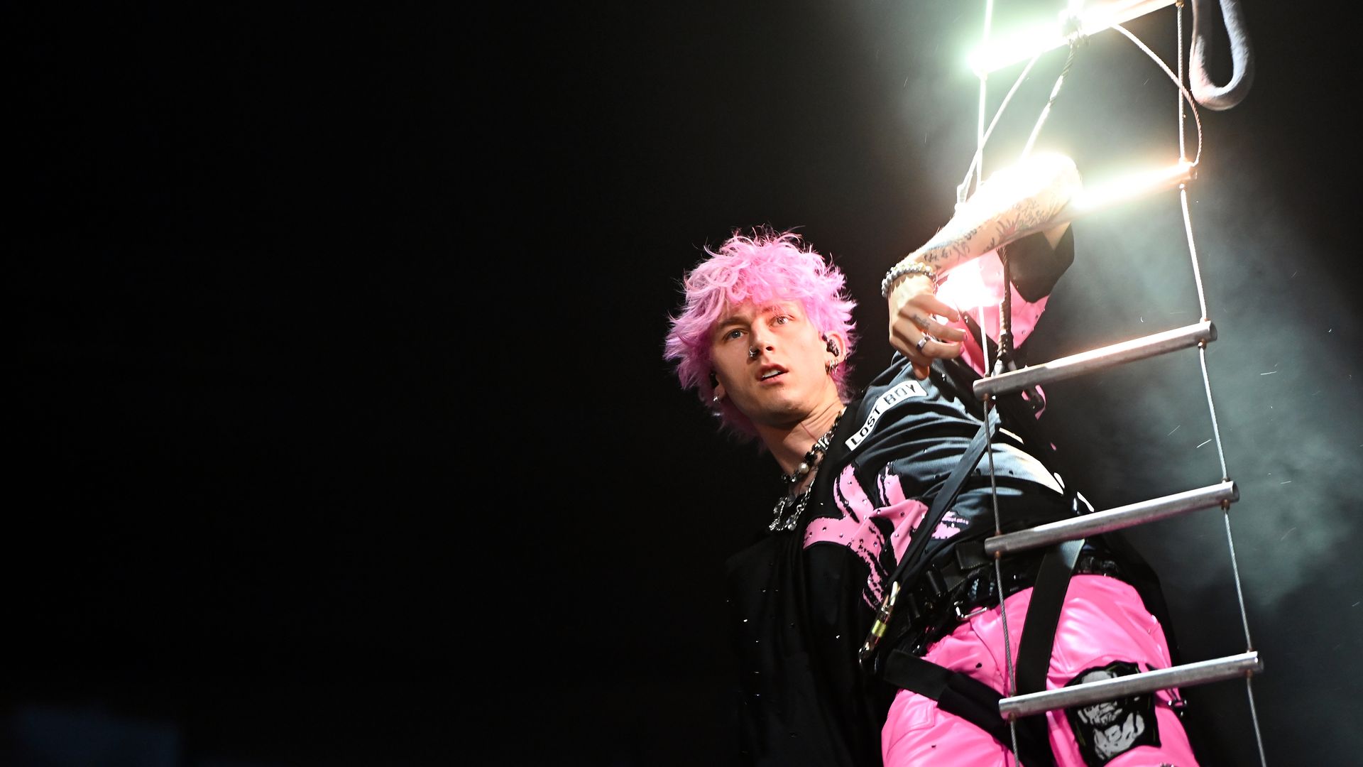 Musician Machine Gun Kelly holds on to a latter extended from a helicopter. 