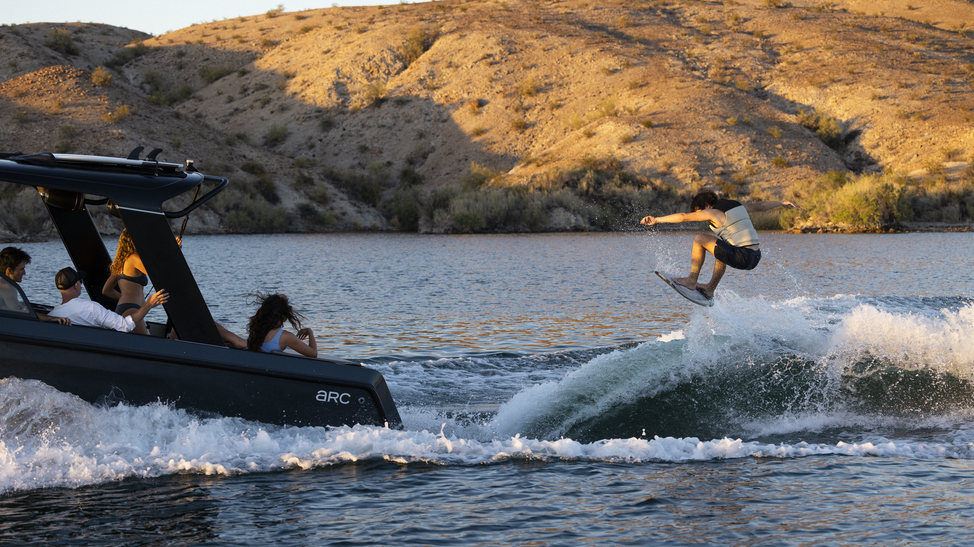 Surfer riding a wave behind the Arc Sport electric boat
