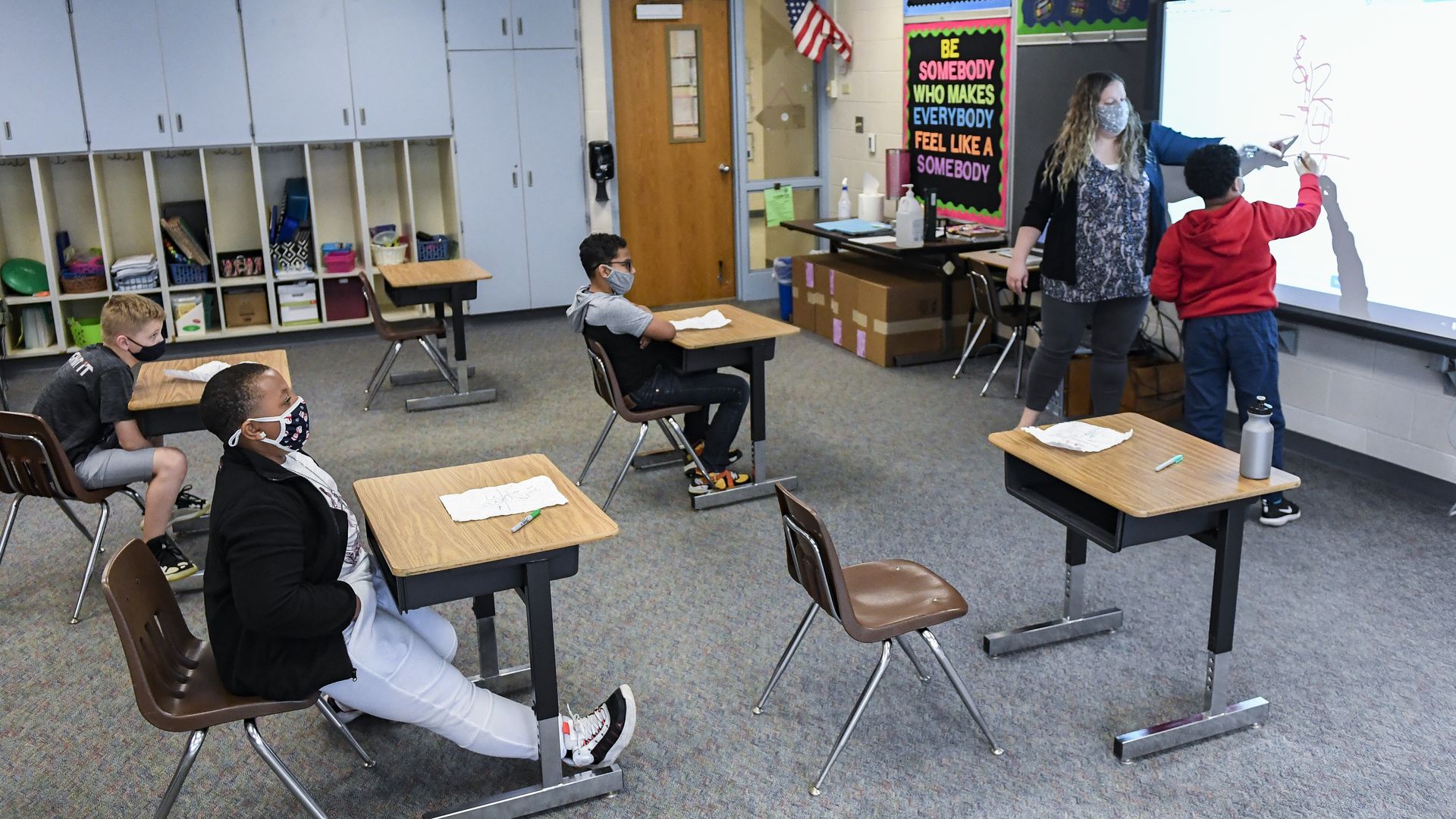 Picture of a classroom with four children sitting socially distanced while wearing masks