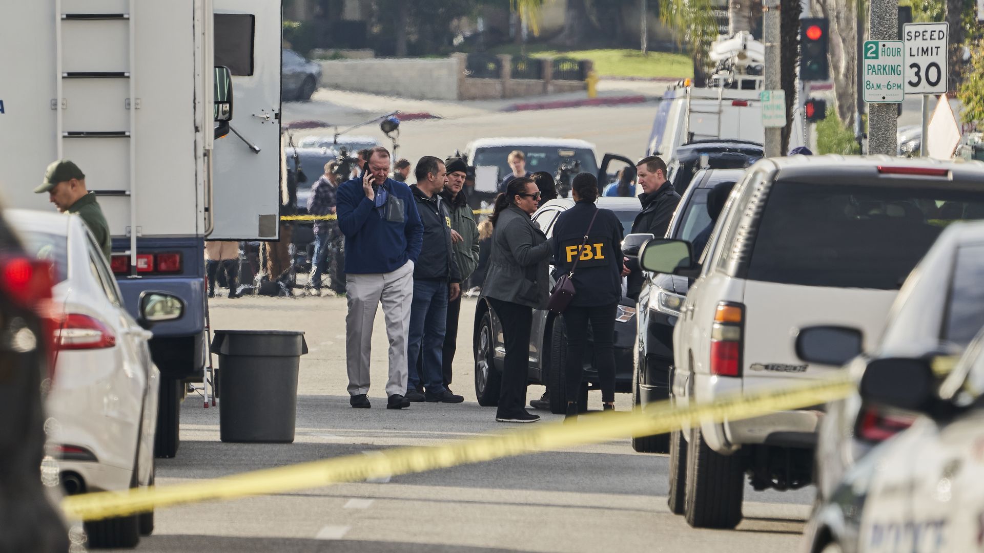 FBI investigators gather in between cars and palm trees on a street during the day in Monterey Park, California in the wake of a mass shooting.