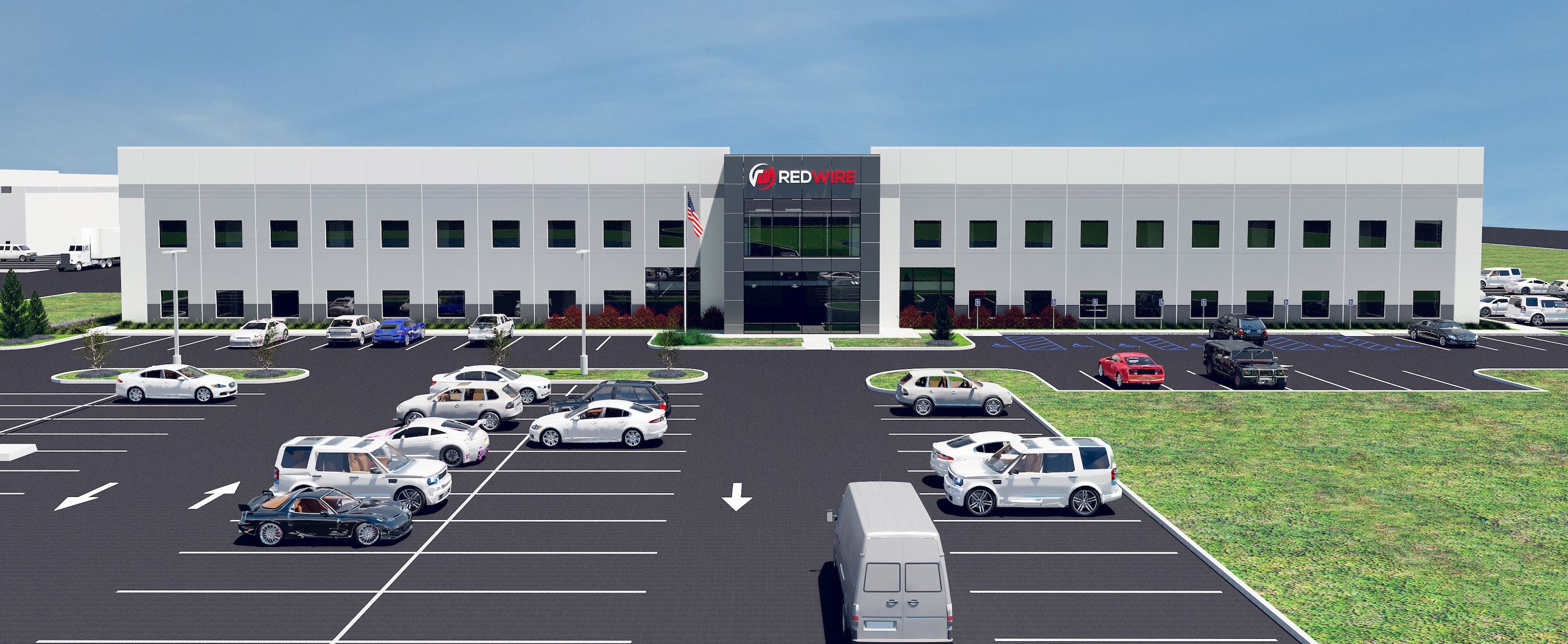 Modern two-story office building with a sign reading RED WIRE, glass entry, and a large parking lot full of cars under a clear blue sky; an American flag near the entrance.