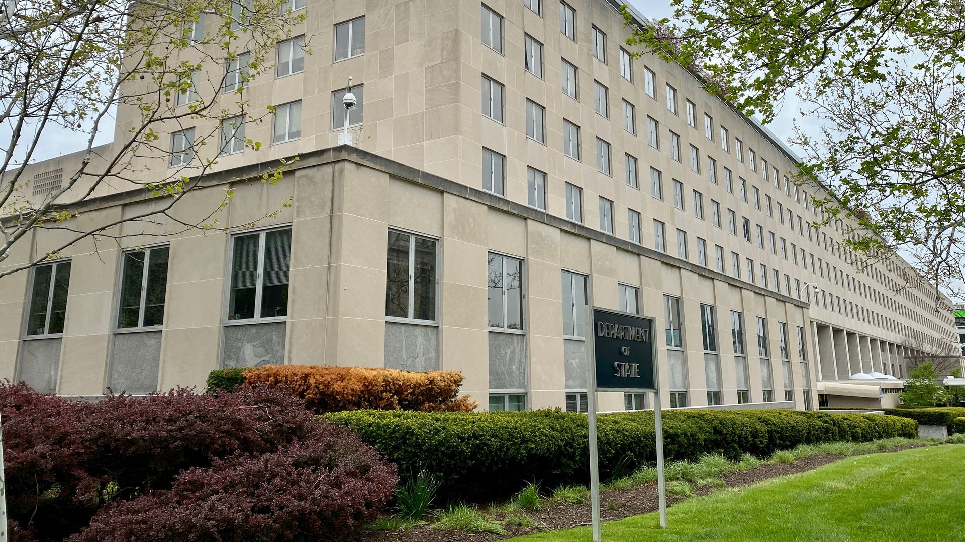 Photo of the Department of State building with a sign engraved with its name in the front lawn
