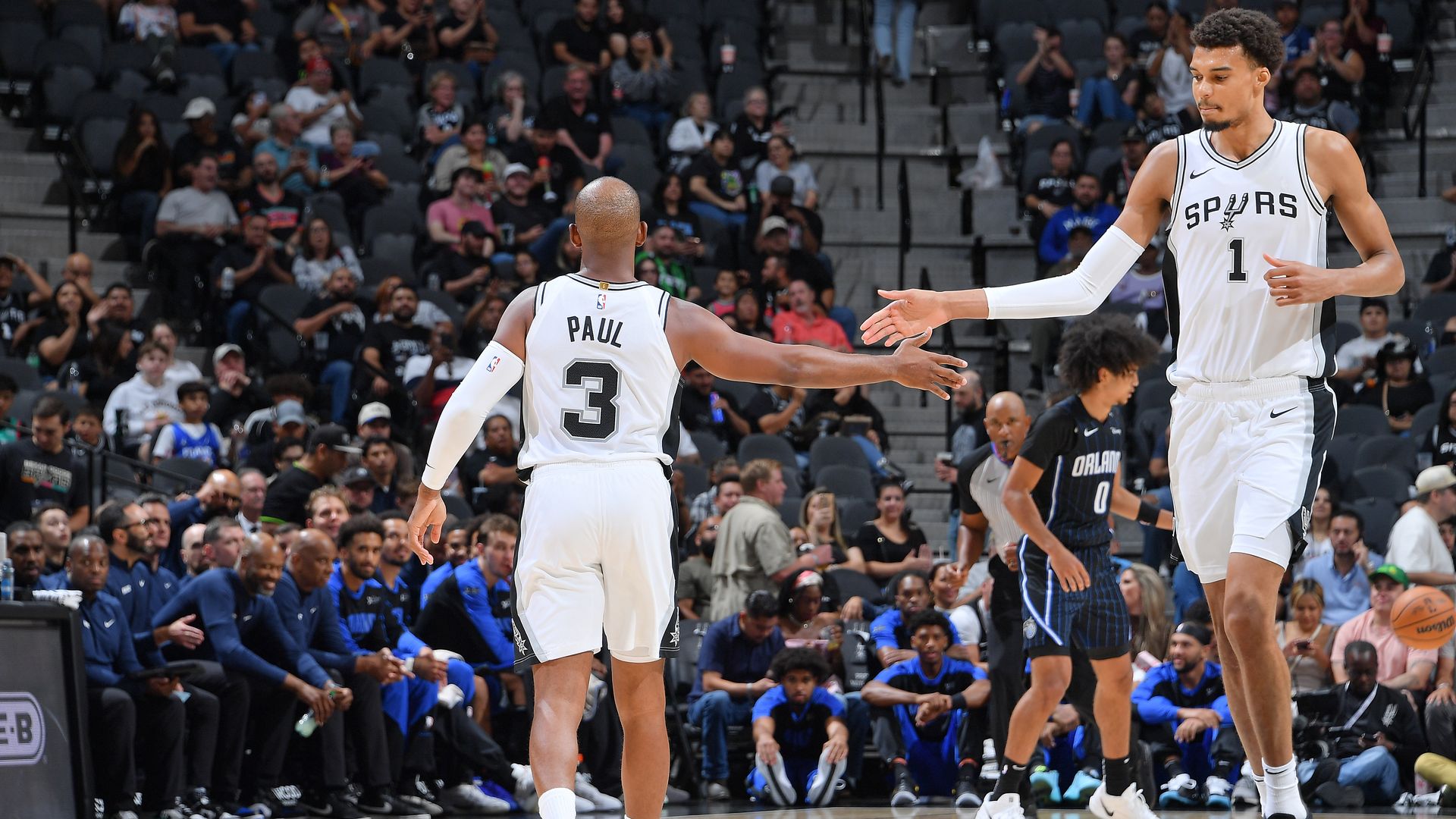 Victor Wembanyama and Chris Paul slap hands on the court during a game. 