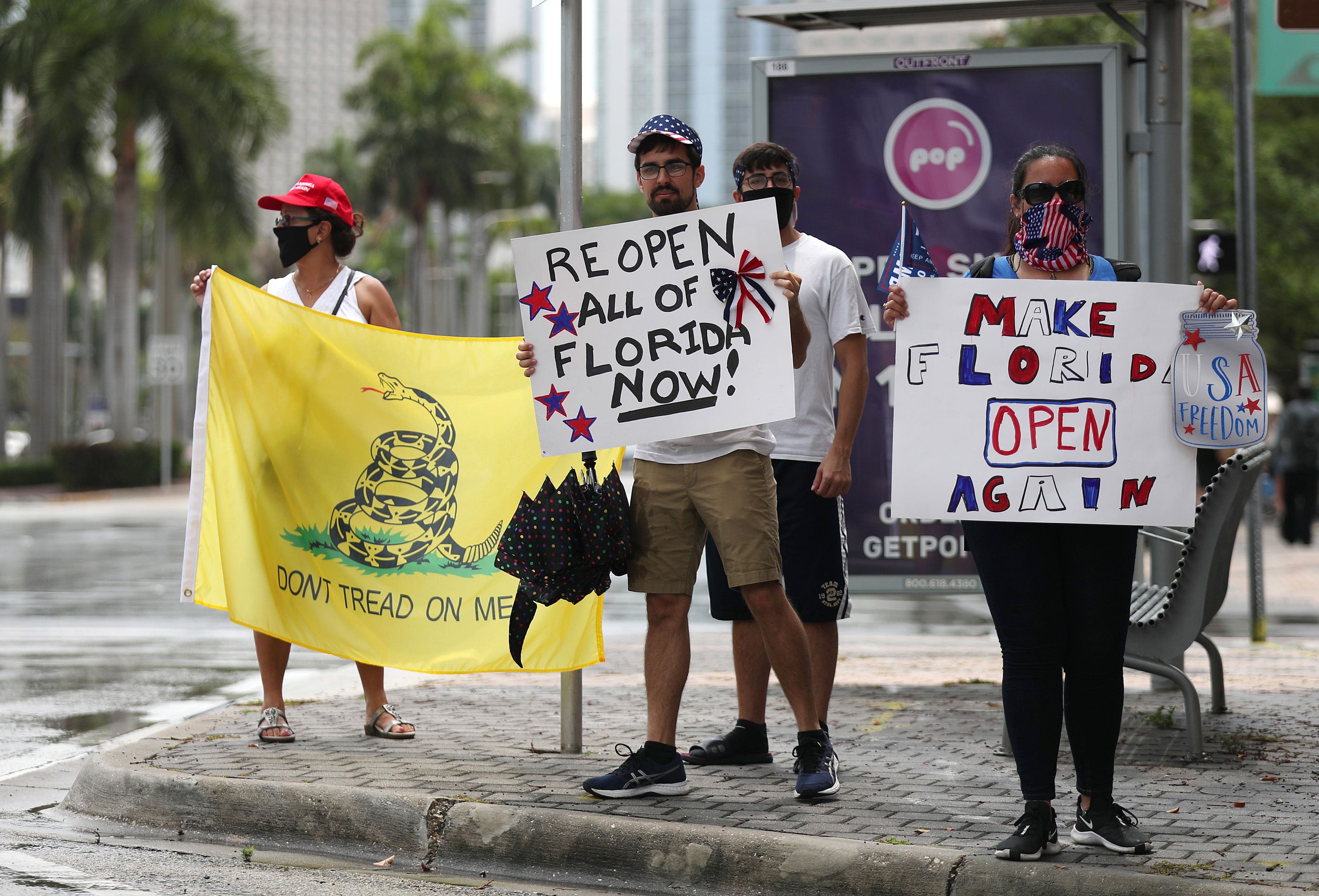 In this image, three signs are held by protestors: one reads "Make Florida open again" another reads "reopen all of florida now" and another reads "don't tread on me"