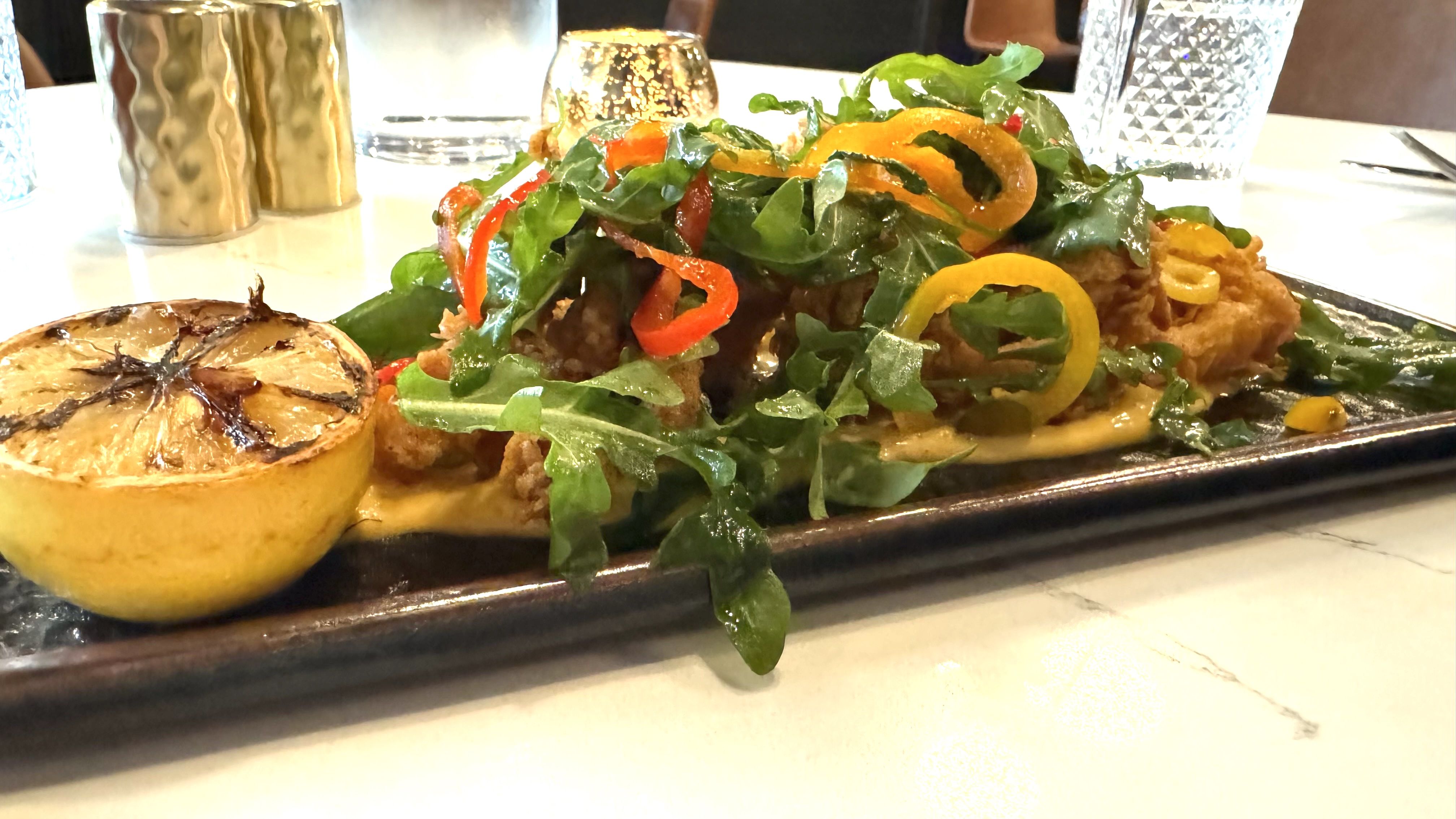 A plate of greens and peppers topping fried calamari. 