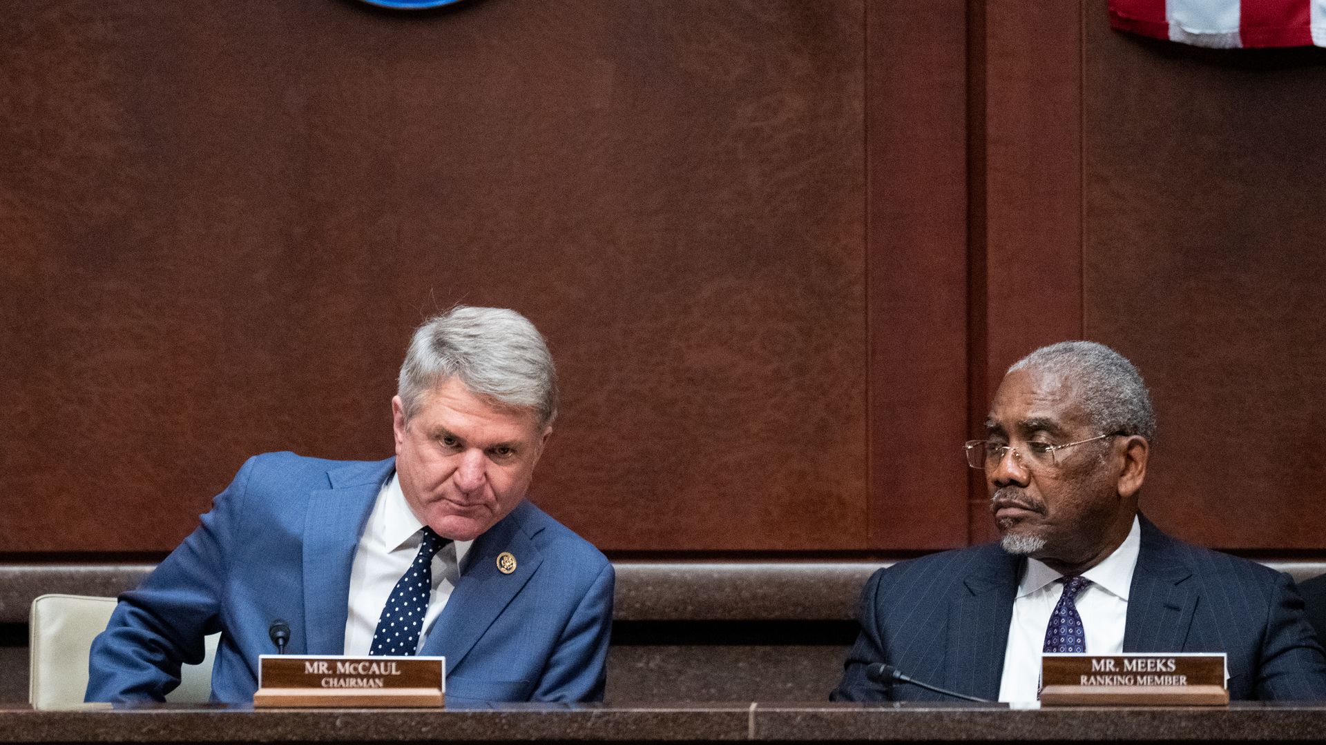 Reps. Michael McCaul, wearing a light blue suit, and Greg Meeks, wearing a dark blue suit, sitting at a marble committee dais in front of a wood-paneled wall.