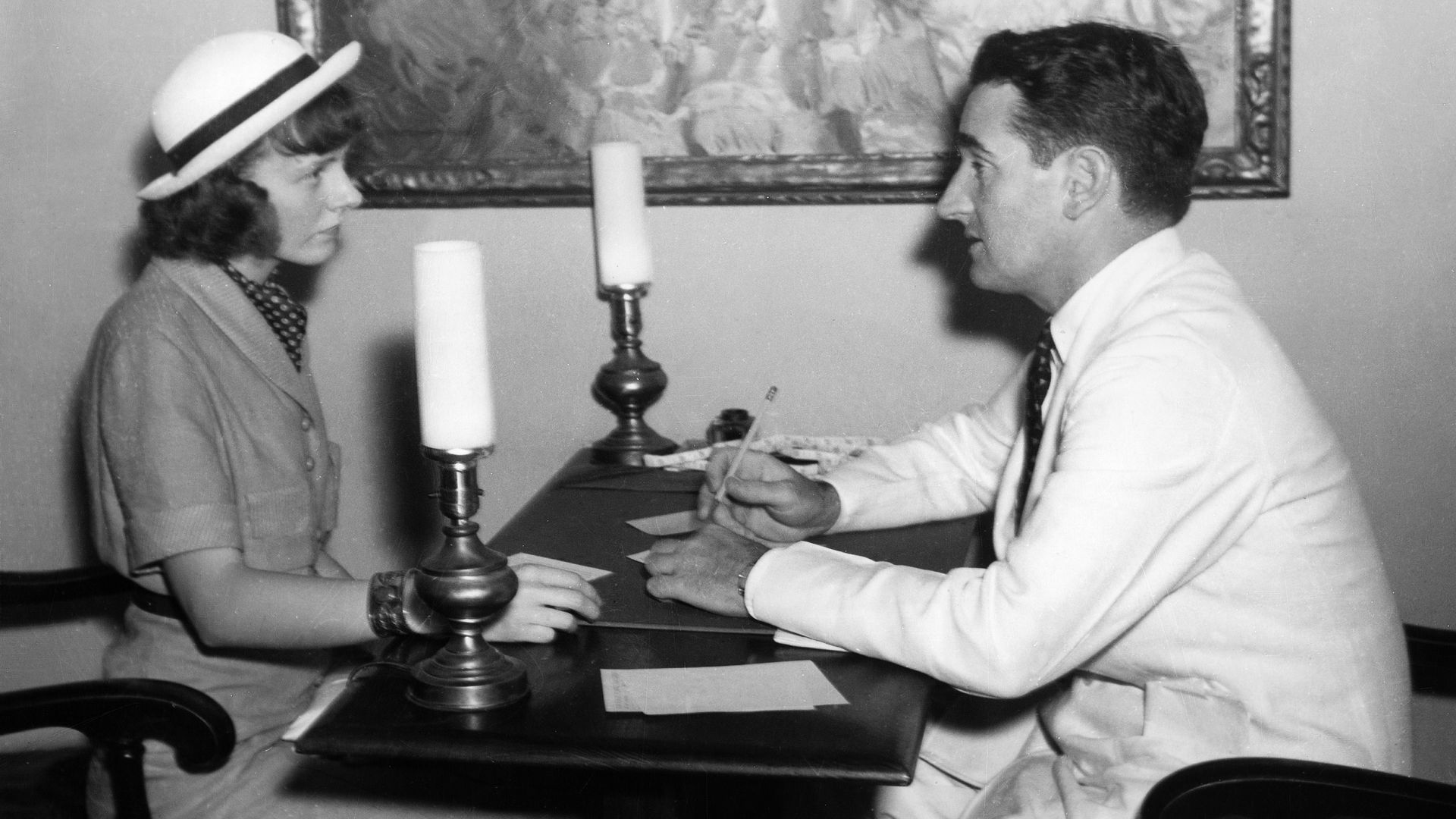 A black and white photo of a man and a woman conversing across a table