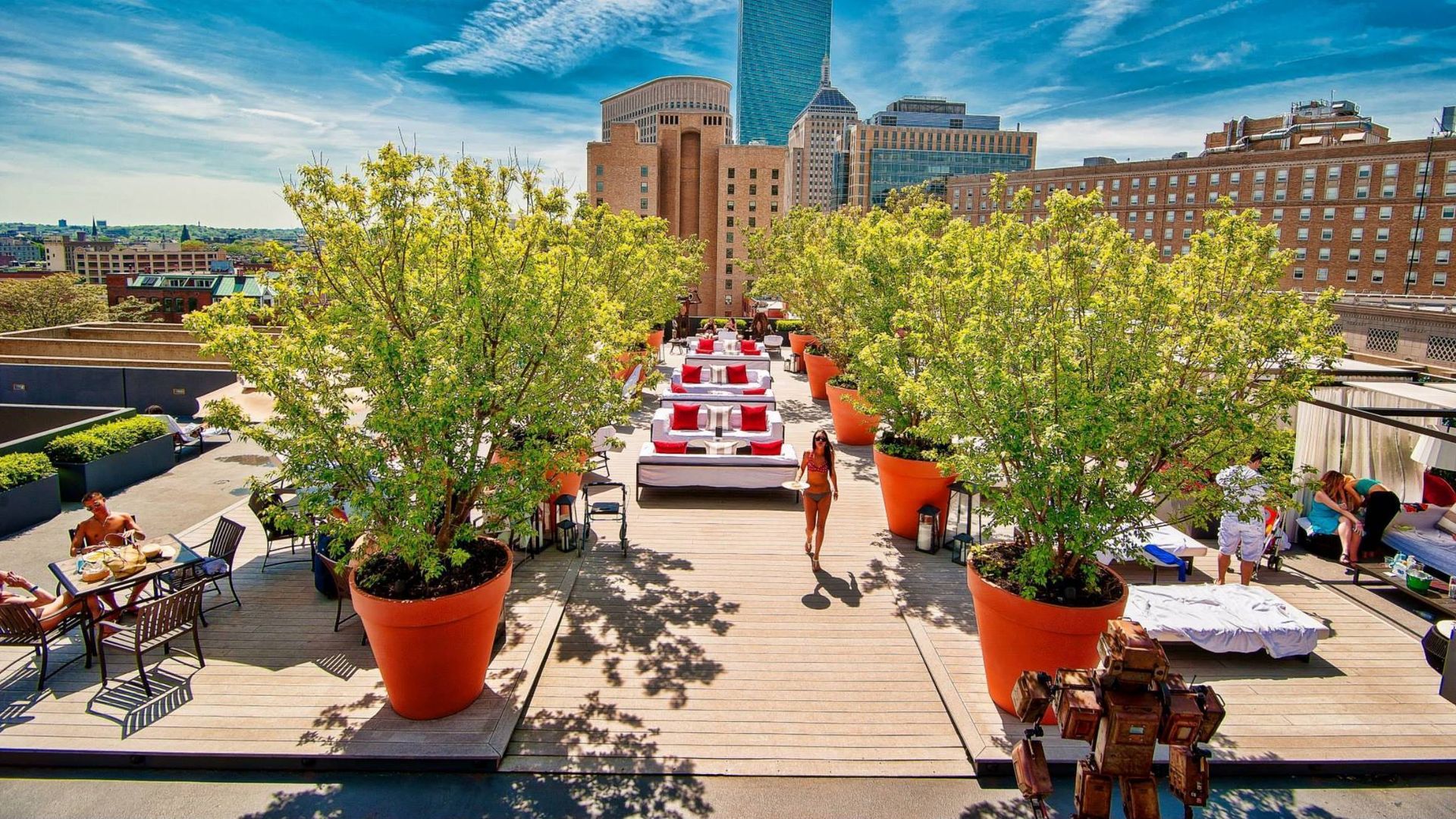 Rooftop@Revere, the rooftop lounge above the Revere Hotel in Boston, has large trees in orange pots, tables and lounge chairs.