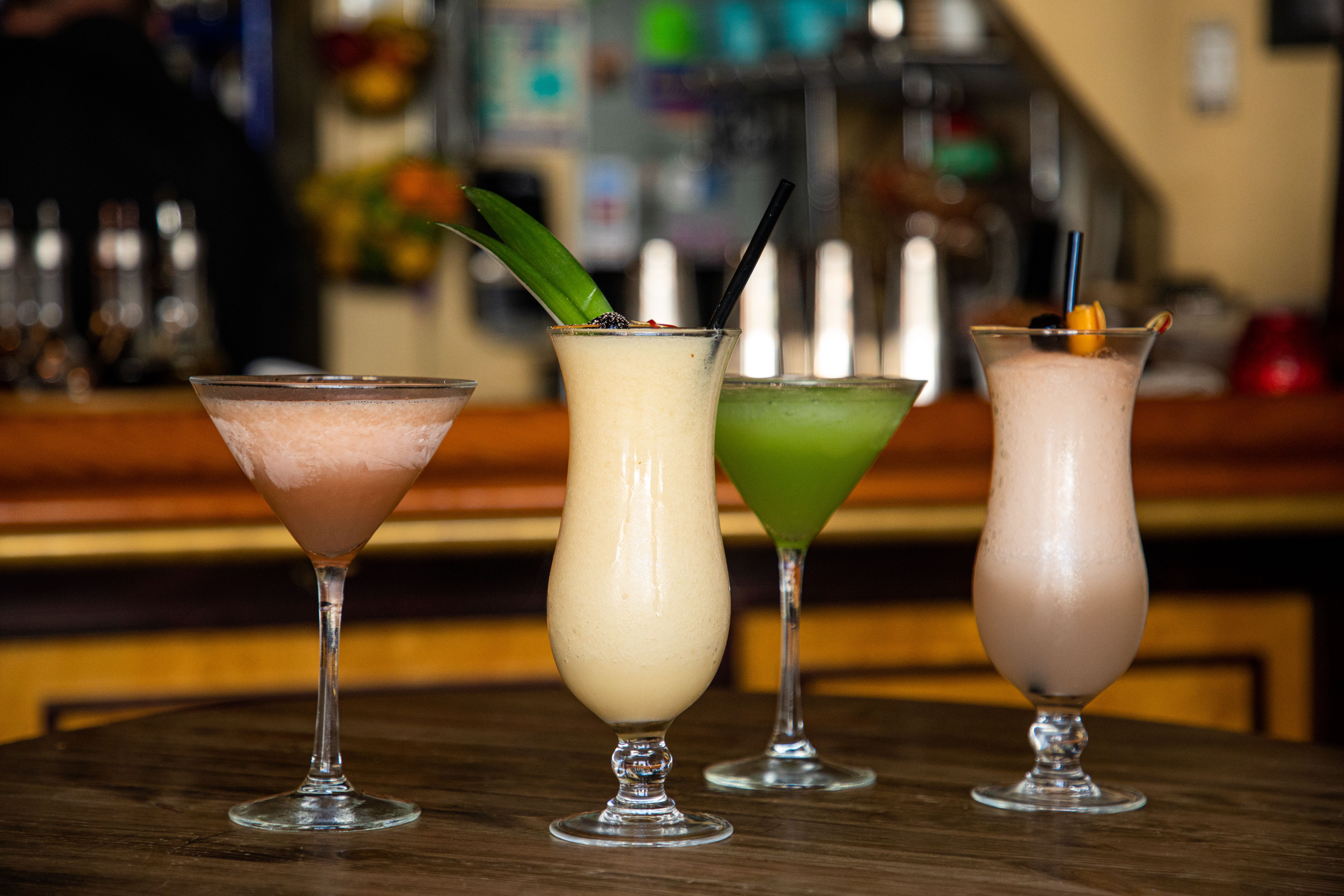 A row of four Cuban cocktails are lined up on a table with a bar out of focus in the background.