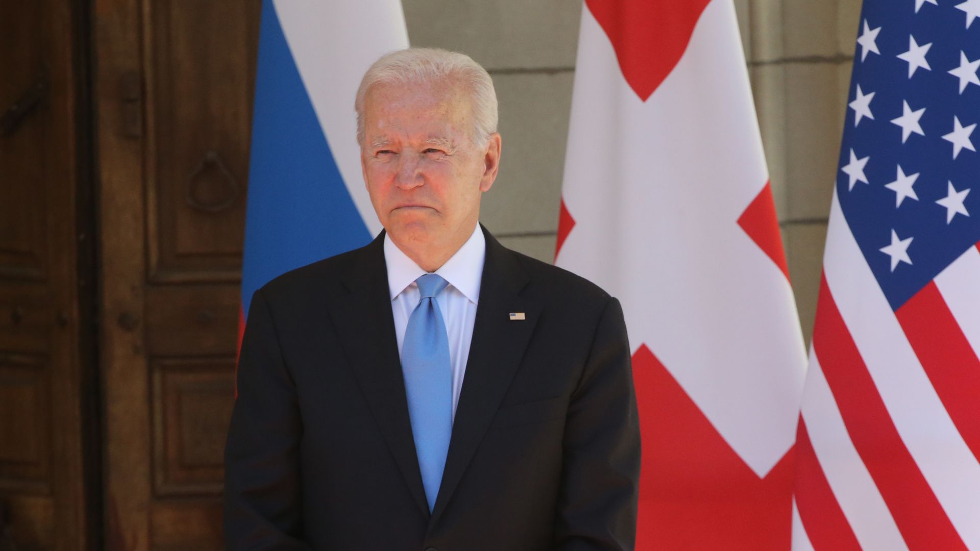 President Biden stands in front of two flags. 