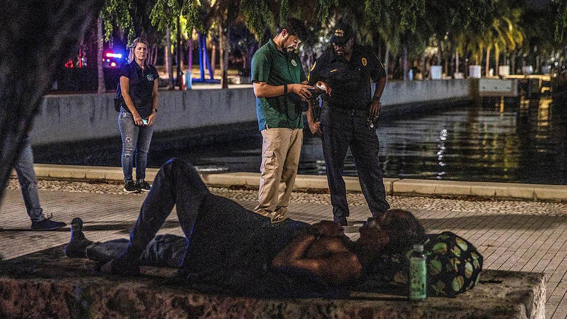 A homeless person sleeps on a city of Miami bench.