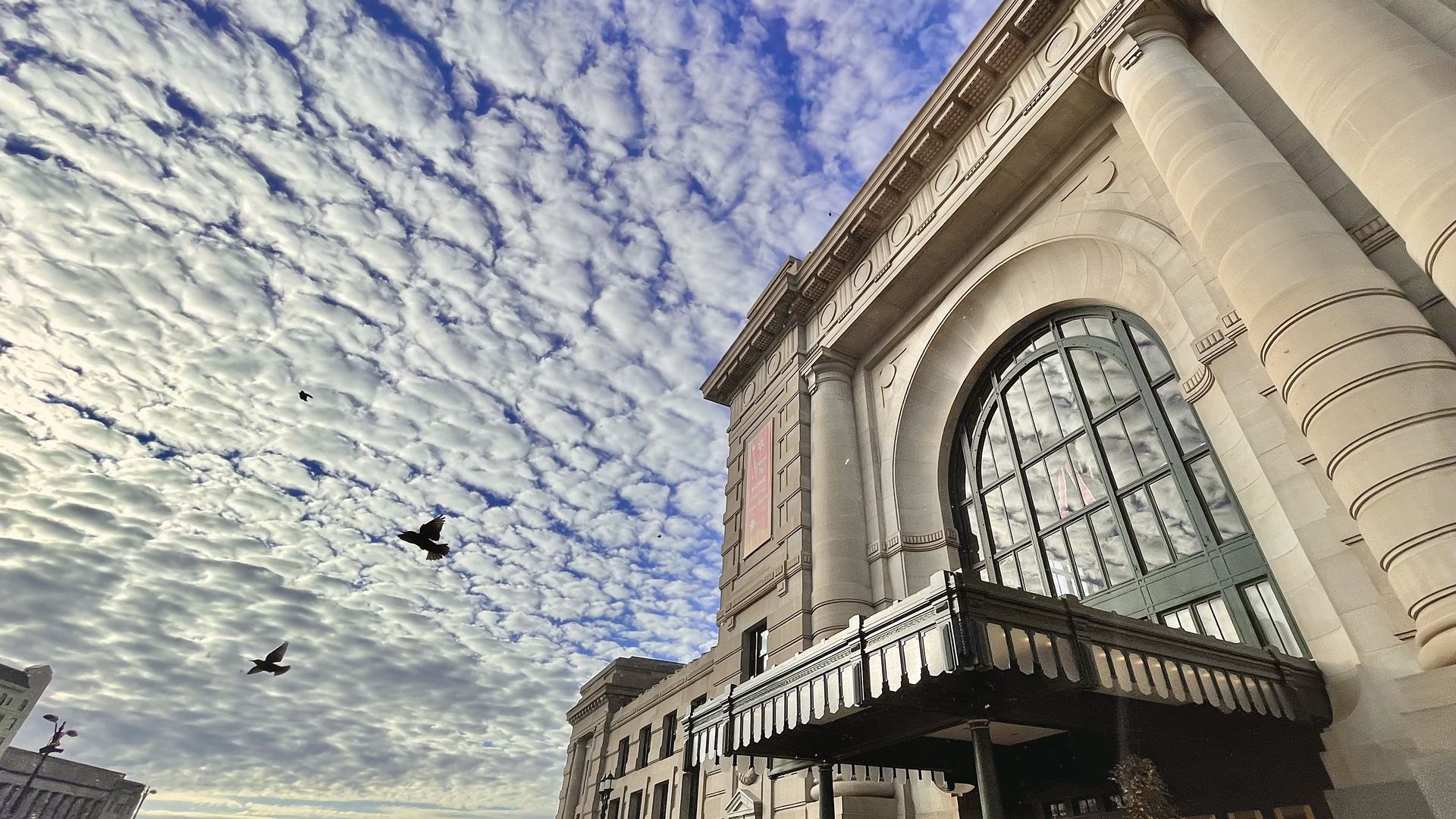 Photo of the facade of Union Station looking up with patterned clouds and birds flying.