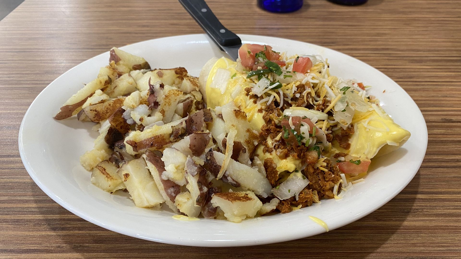 Chopped potatoes and an enchilada covered in cheese and yellow sauce on a white plate. 